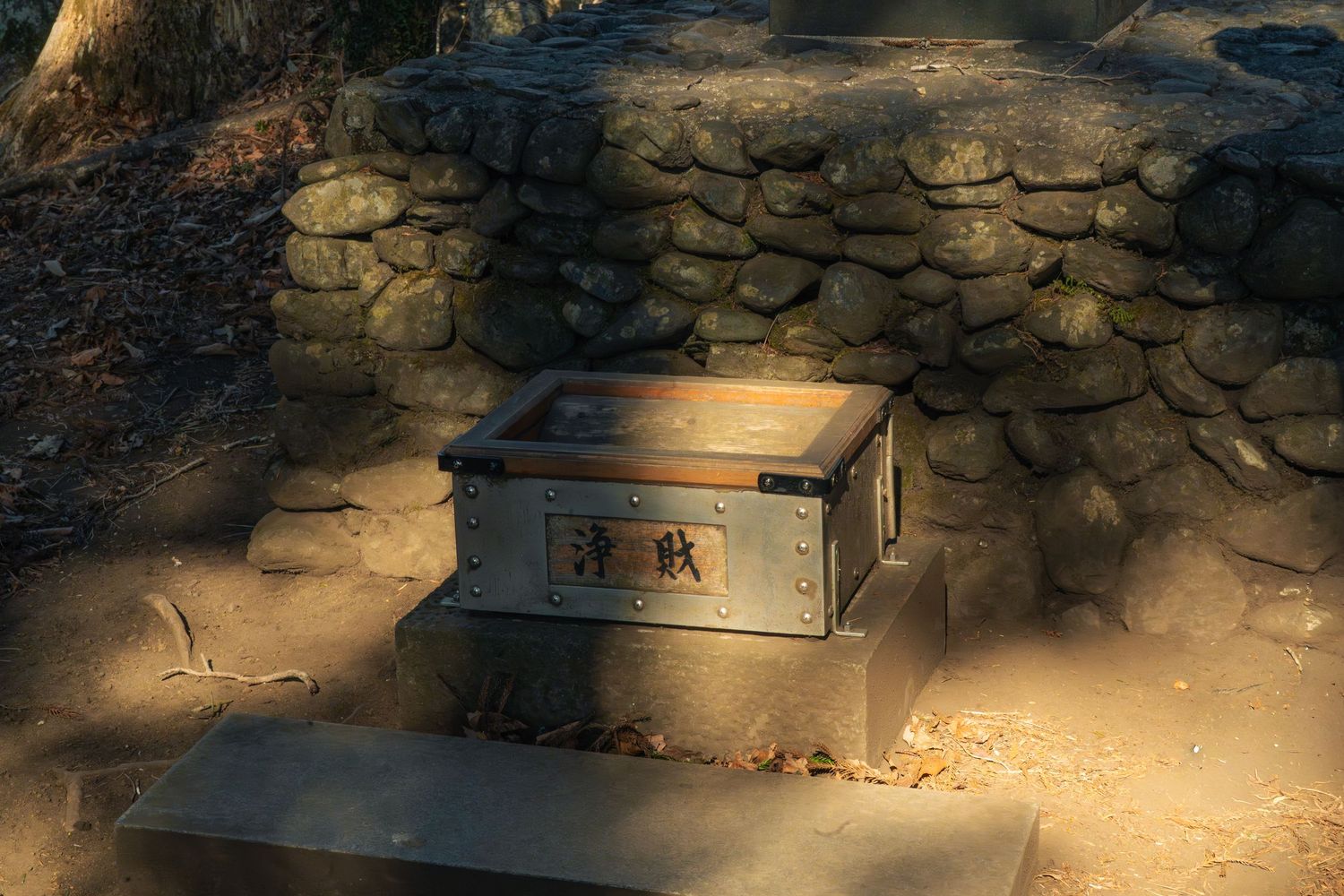 Ancient stone memorial with bronze plaque in sunlit outdoor historical site.