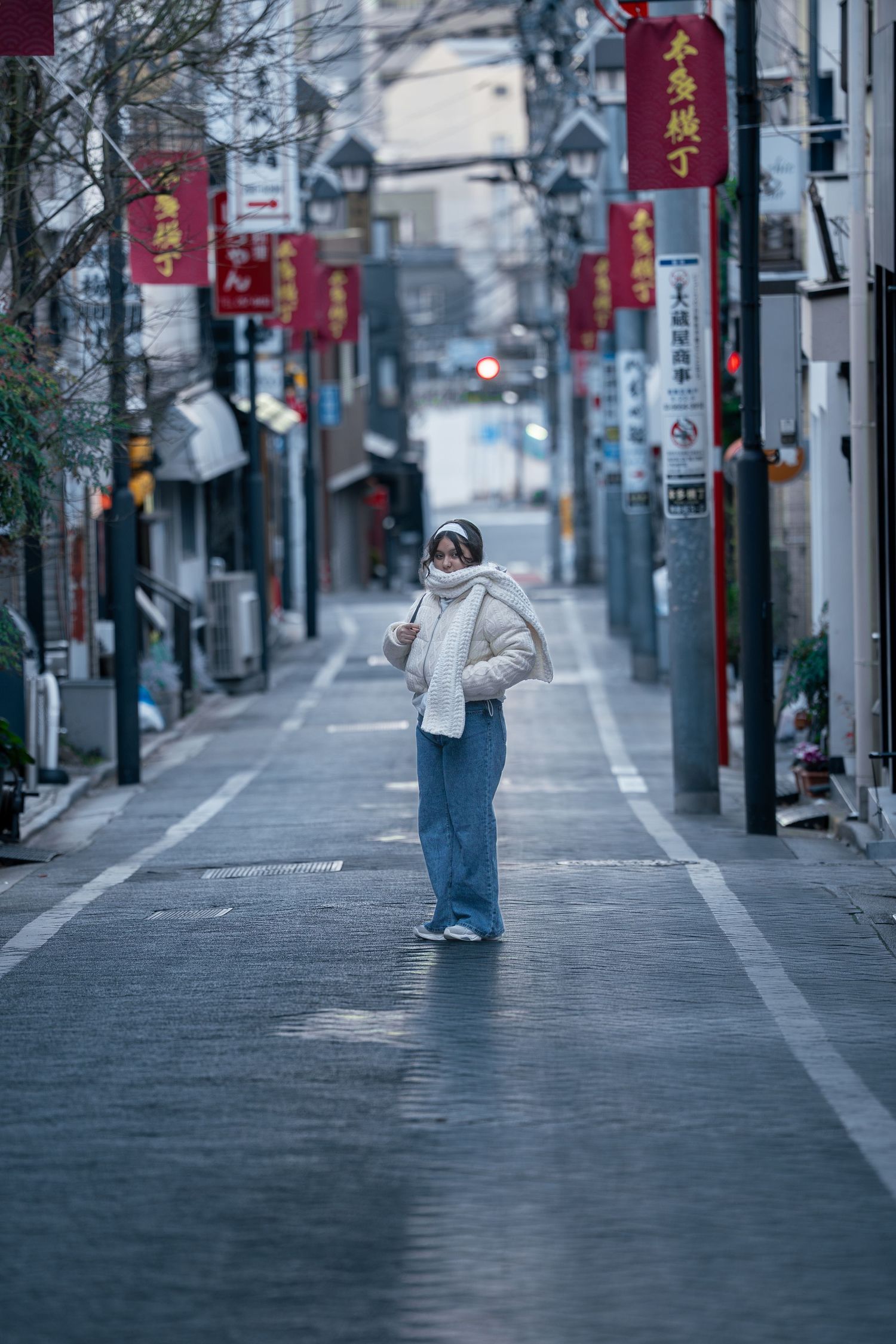 Woman in a white puffer jacket standing alone on a quiet street in a Japanese Chinatown district.