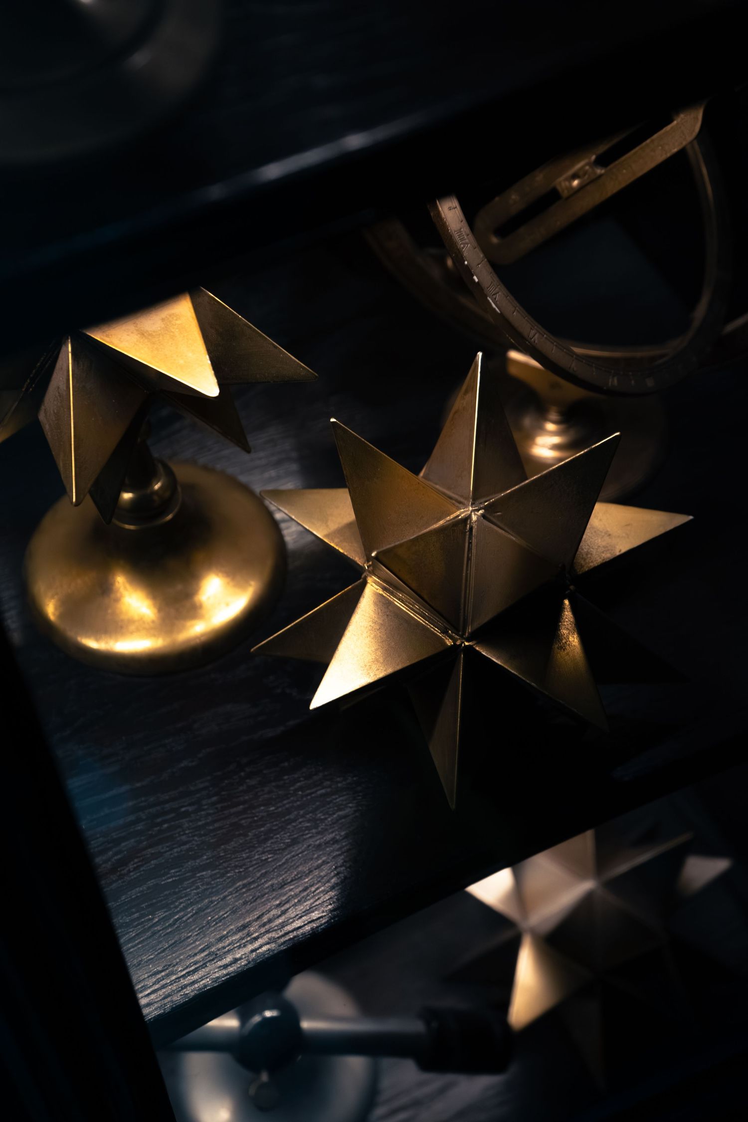 Golden geometric star-shaped decorative objects arranged on dark wooden surface in dramatic lighting.