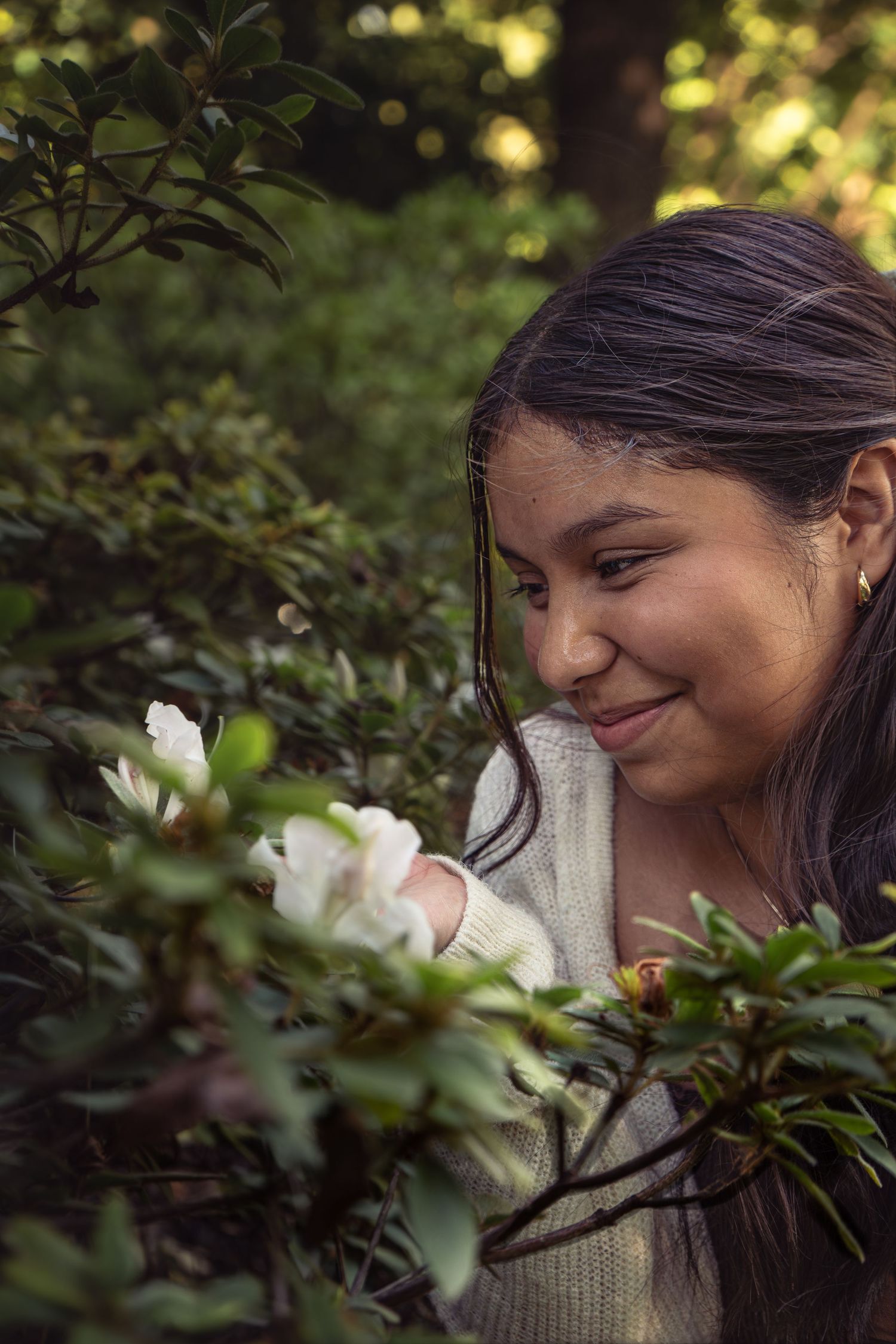Young woman smiling while admiring white flowers blooming in a lush green garden.