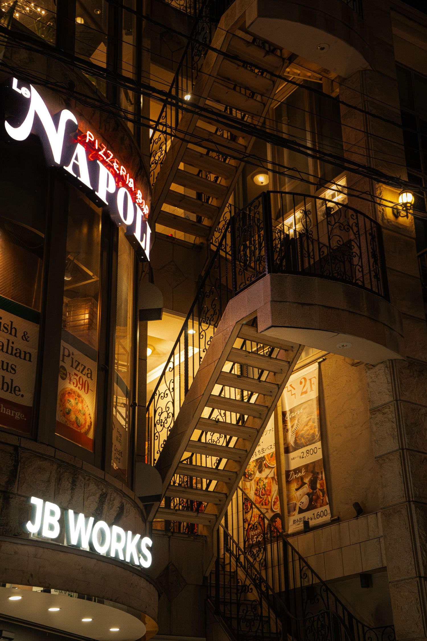 Illuminated Napoli pizzeria restaurant exterior at night with iron staircase and JB Works sign.