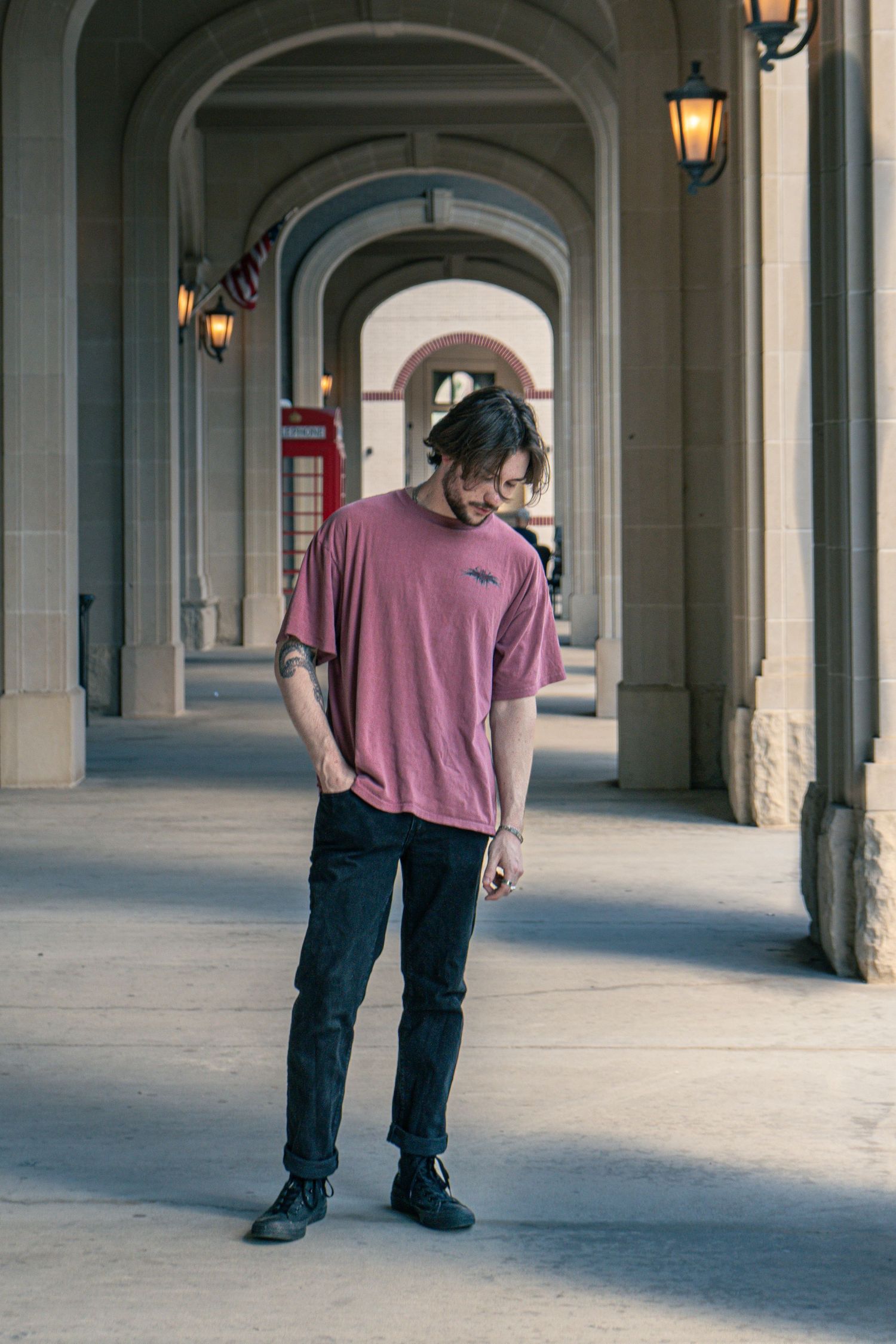 Man in pink oversized t-shirt standing in an arched corridor with hanging lanterns.