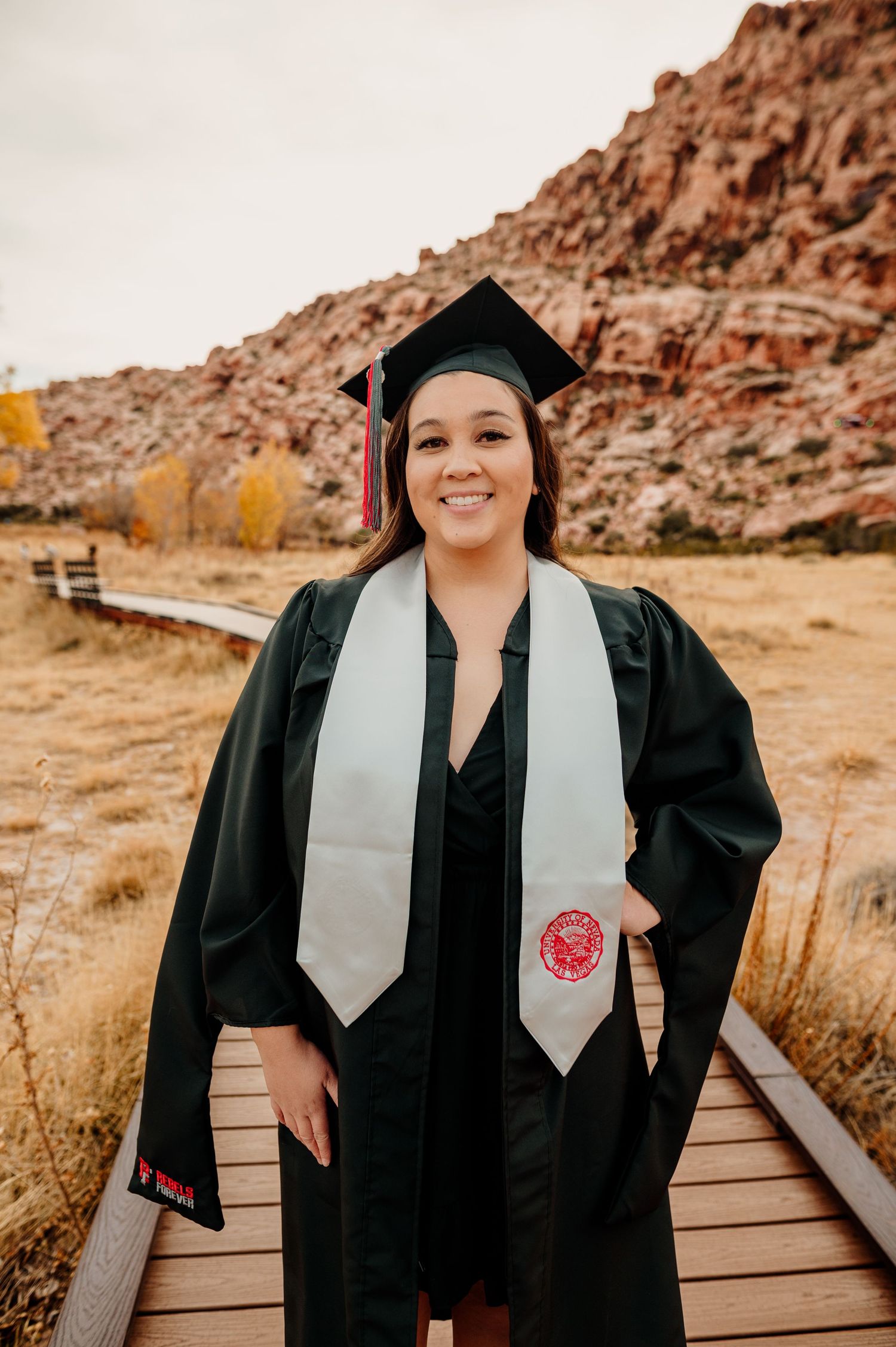 Smiling female graduate in black cap and gown with white stole at Red Rock Canyon.