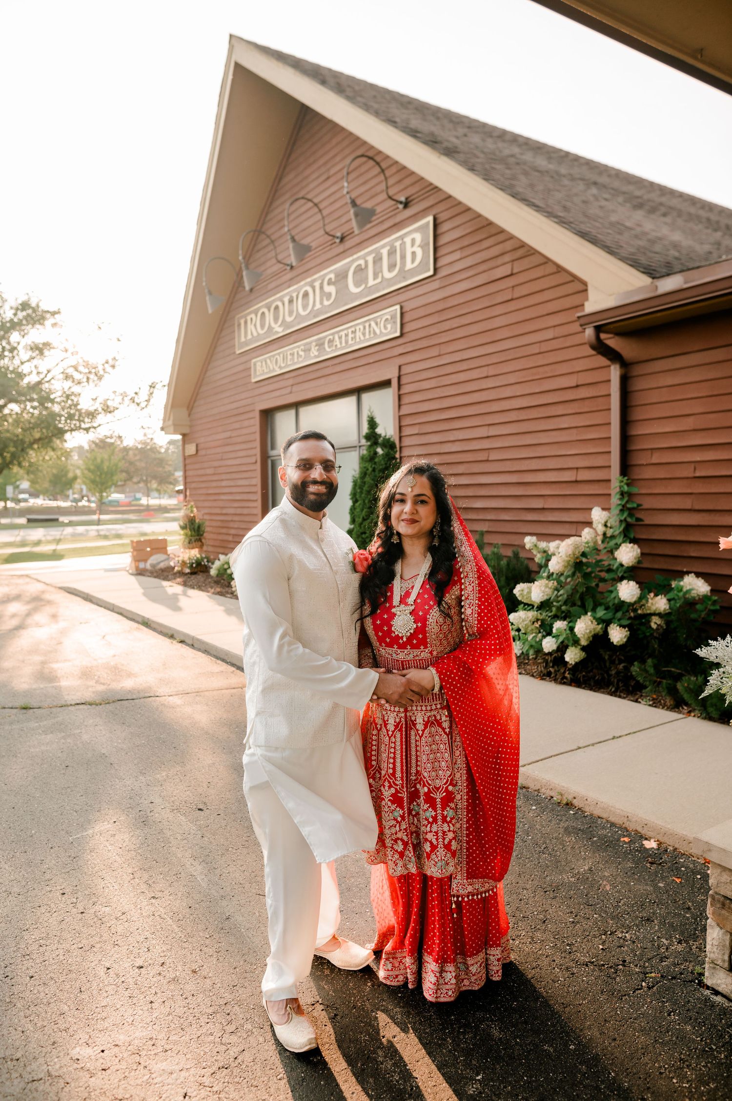 Couple in traditional South Asian wedding attire pose outside Iroquois Club banquet hall on their wedding day.