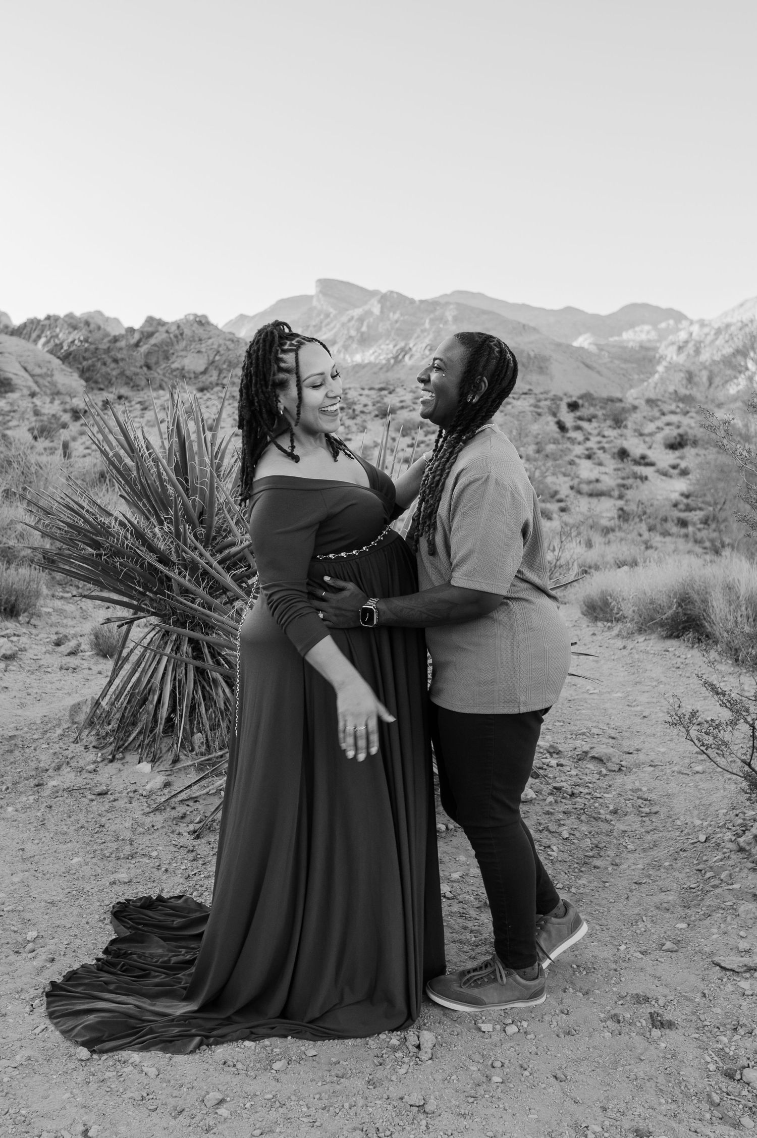 Black and white maternity photo of two women embracing in desert mountain landscape.