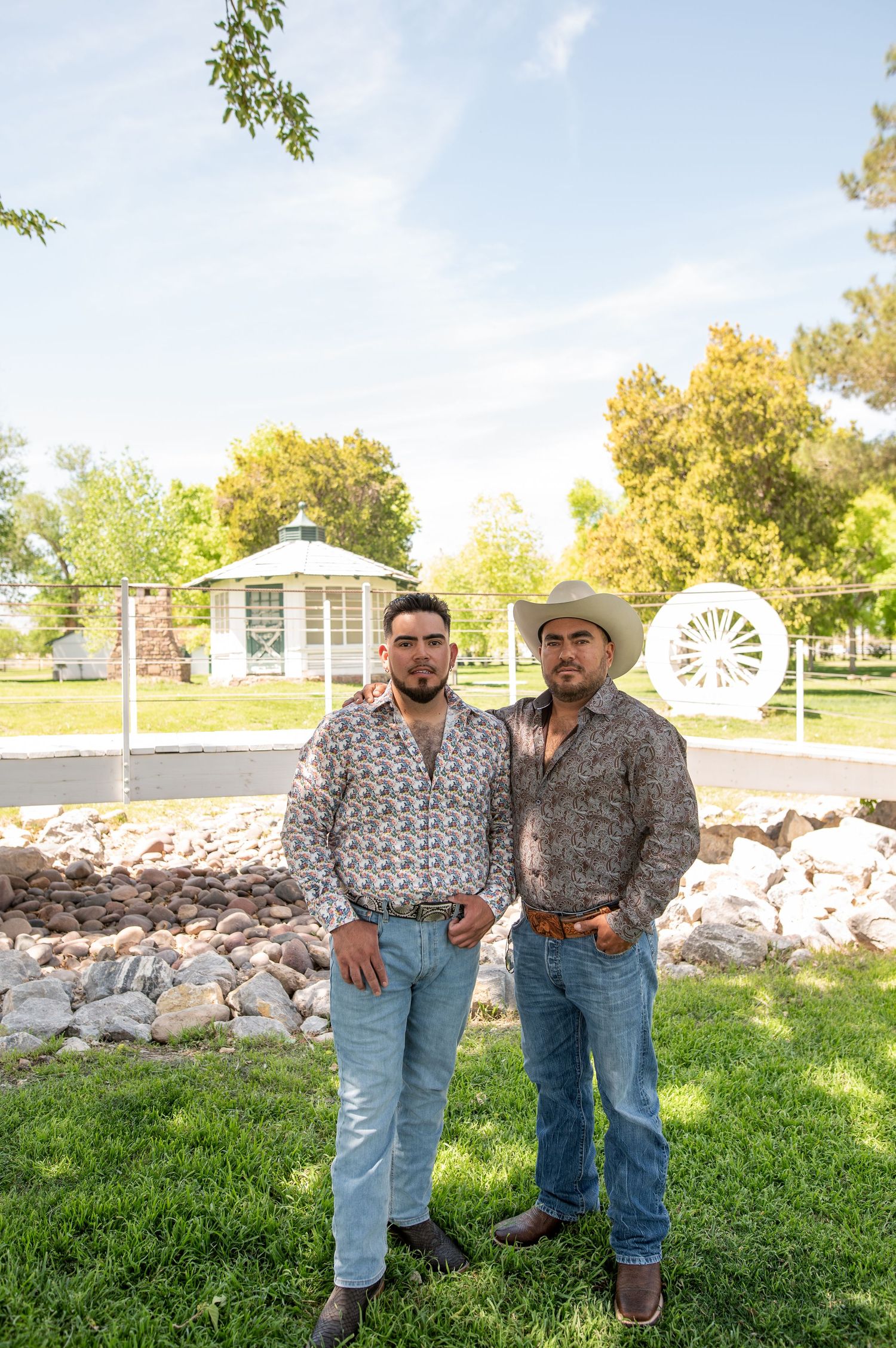 Two young men in patterned western shirts posing in a sunny park.