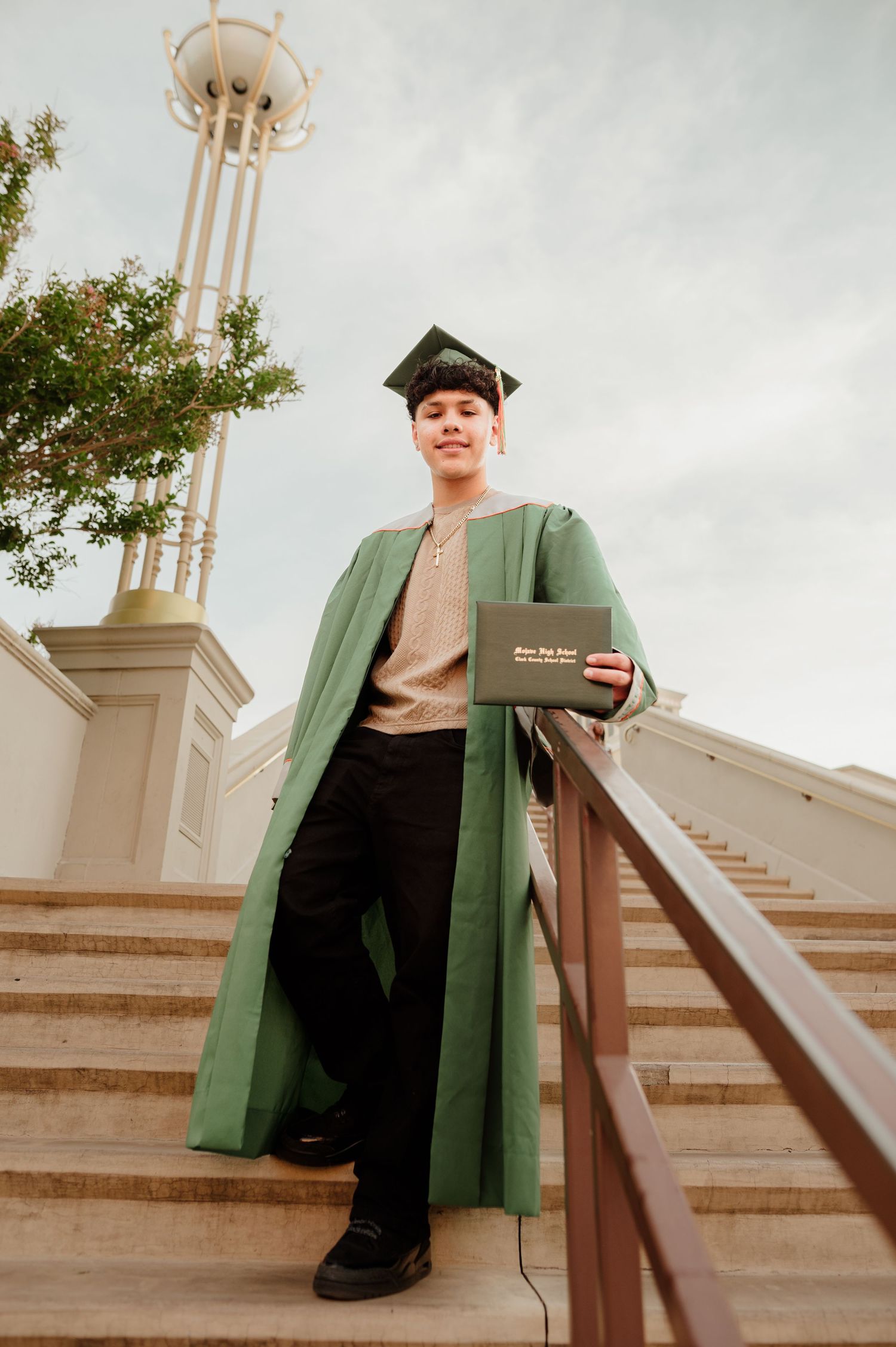 Smiling graduate in green gown holding diploma on steps at Caesars Palace Las Vegas.