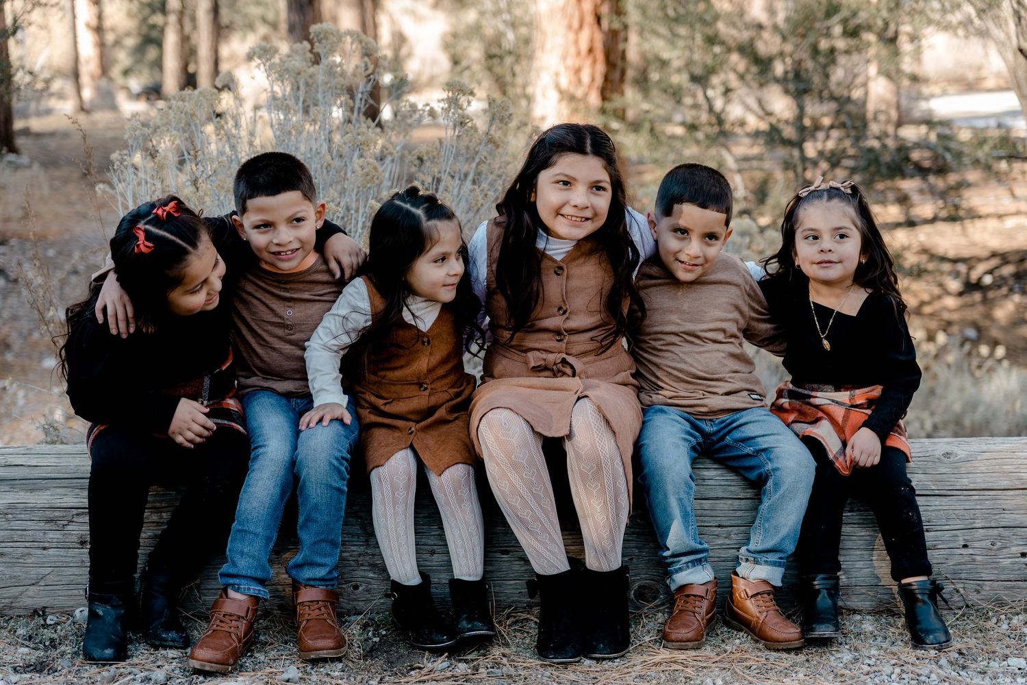 Six children sit together on a wooden bench outdoors, smiling and posing for a group portrait.