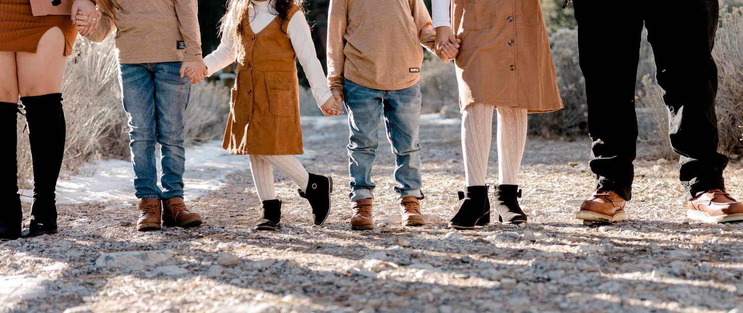 Close-up of a family's feet lined up on a gravel path, wearing coordinated brown and black shoes.