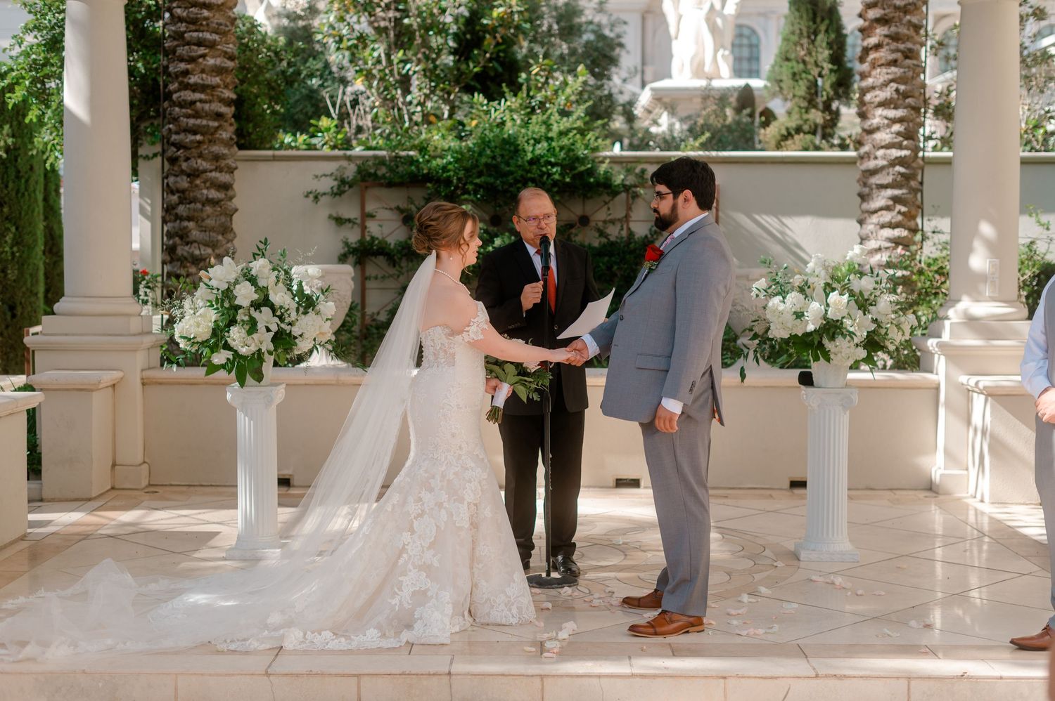 Bride and groom exchange vows at elegant outdoor ceremony with white floral arrangements.