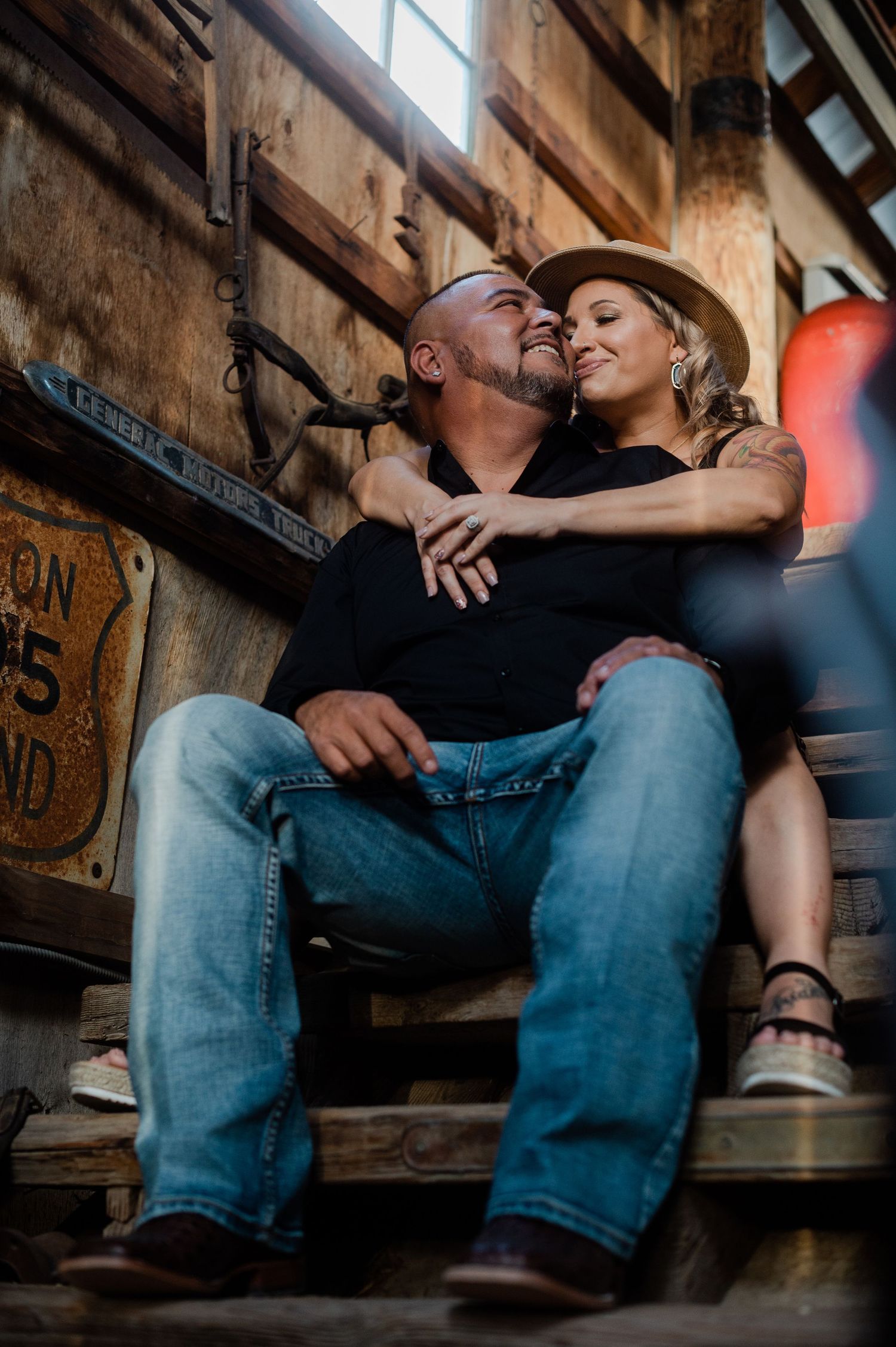 Couple sitting on rustic wooden steps in a barn, sharing an intimate moment together.