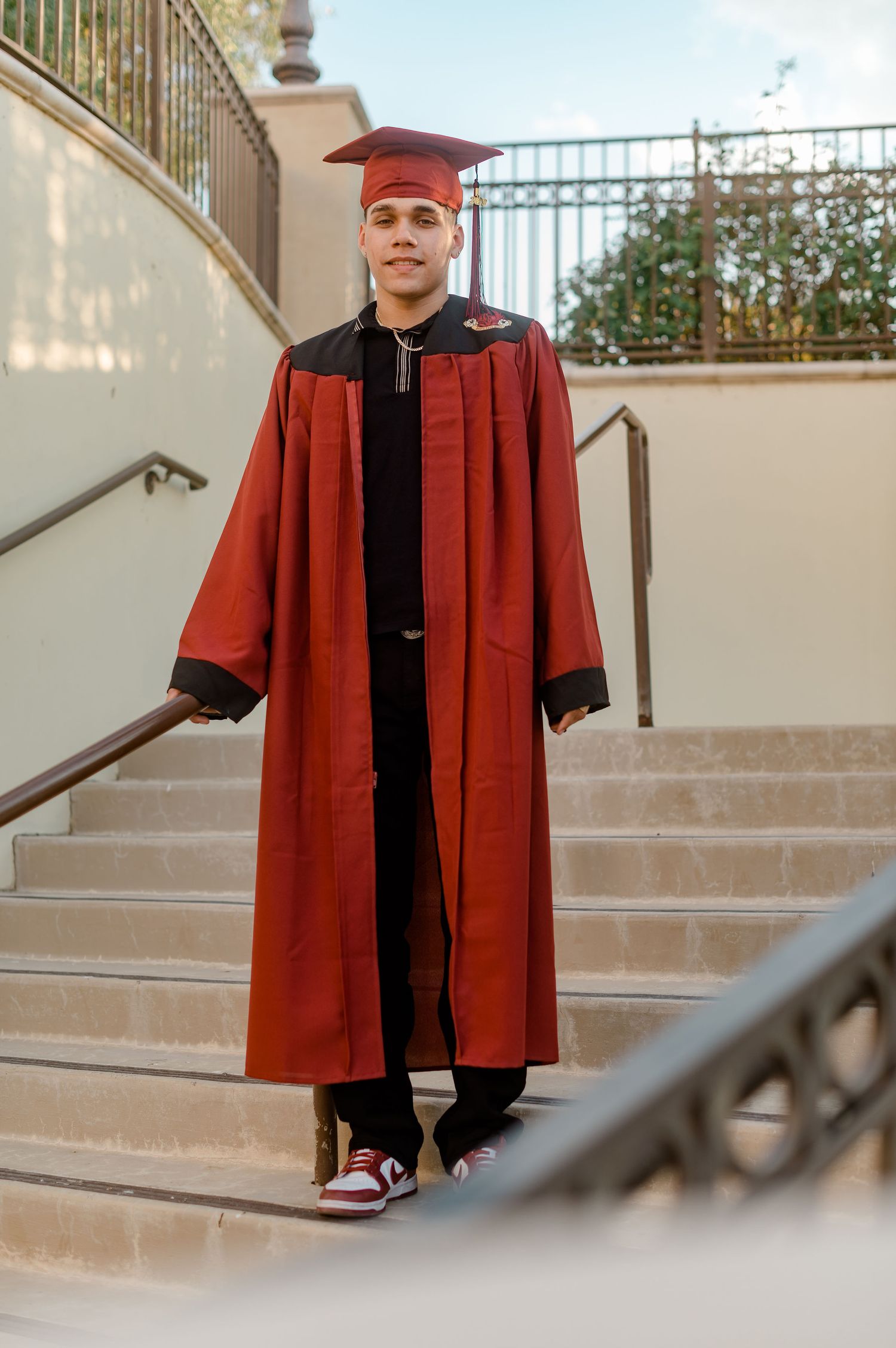 Young man in red graduation cap and gown walking down outdoor stairs.