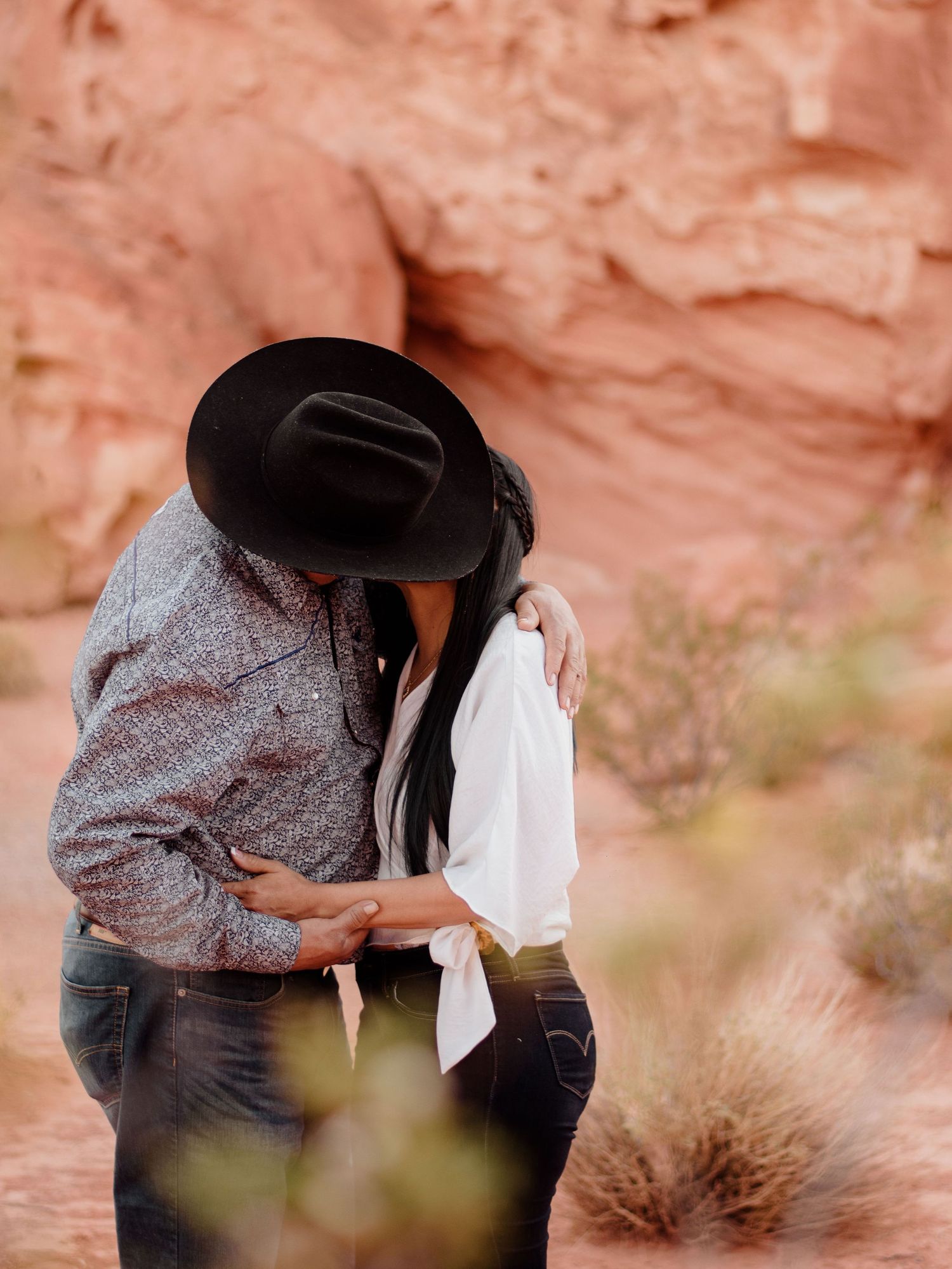 Couple sharing a romantic kiss among red rock formations in a desert landscape.
