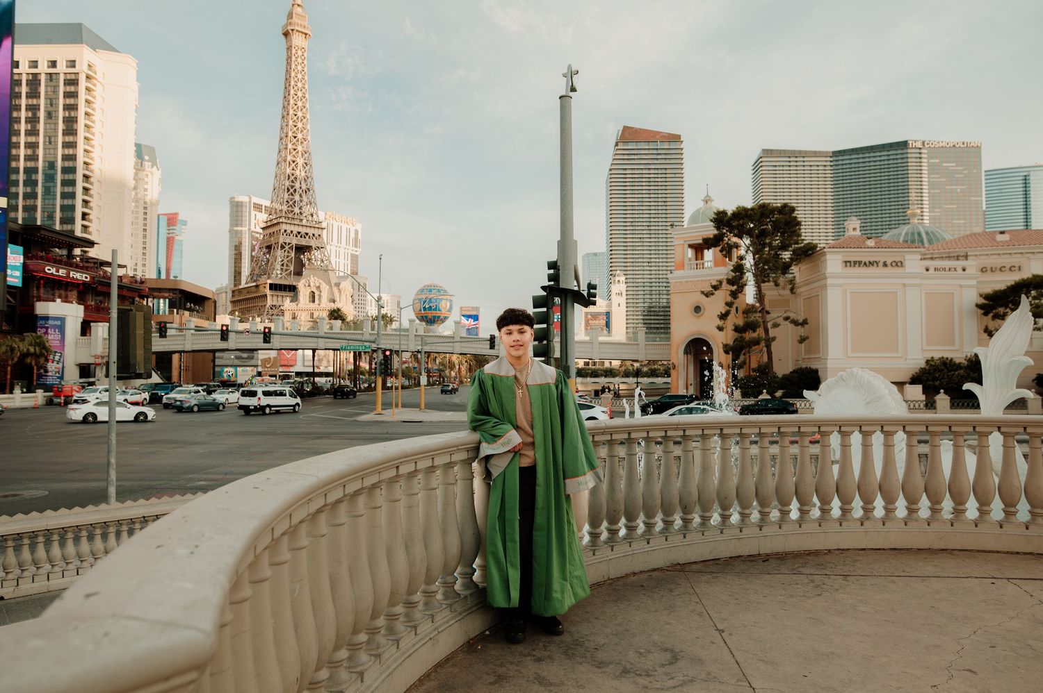 Graduate in green cap and gown posing on Las Vegas Strip with Eiffel Tower replica.