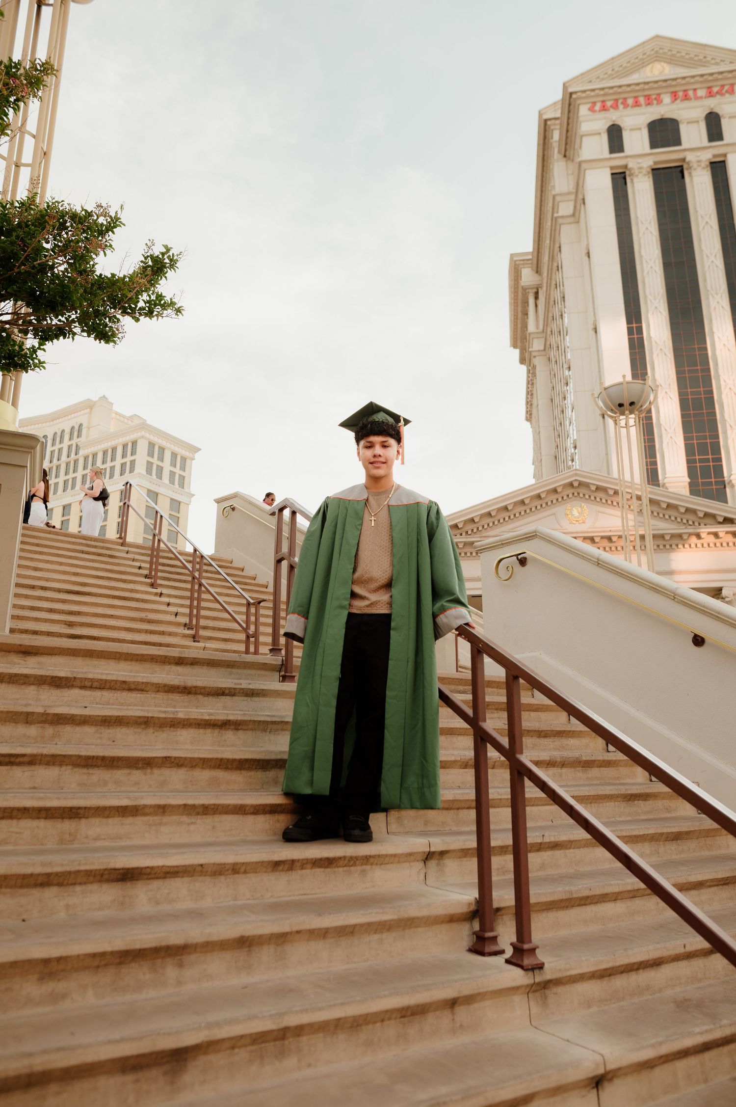 Graduate in green gown and cap on grand staircase outside Caesars Palace Las Vegas.