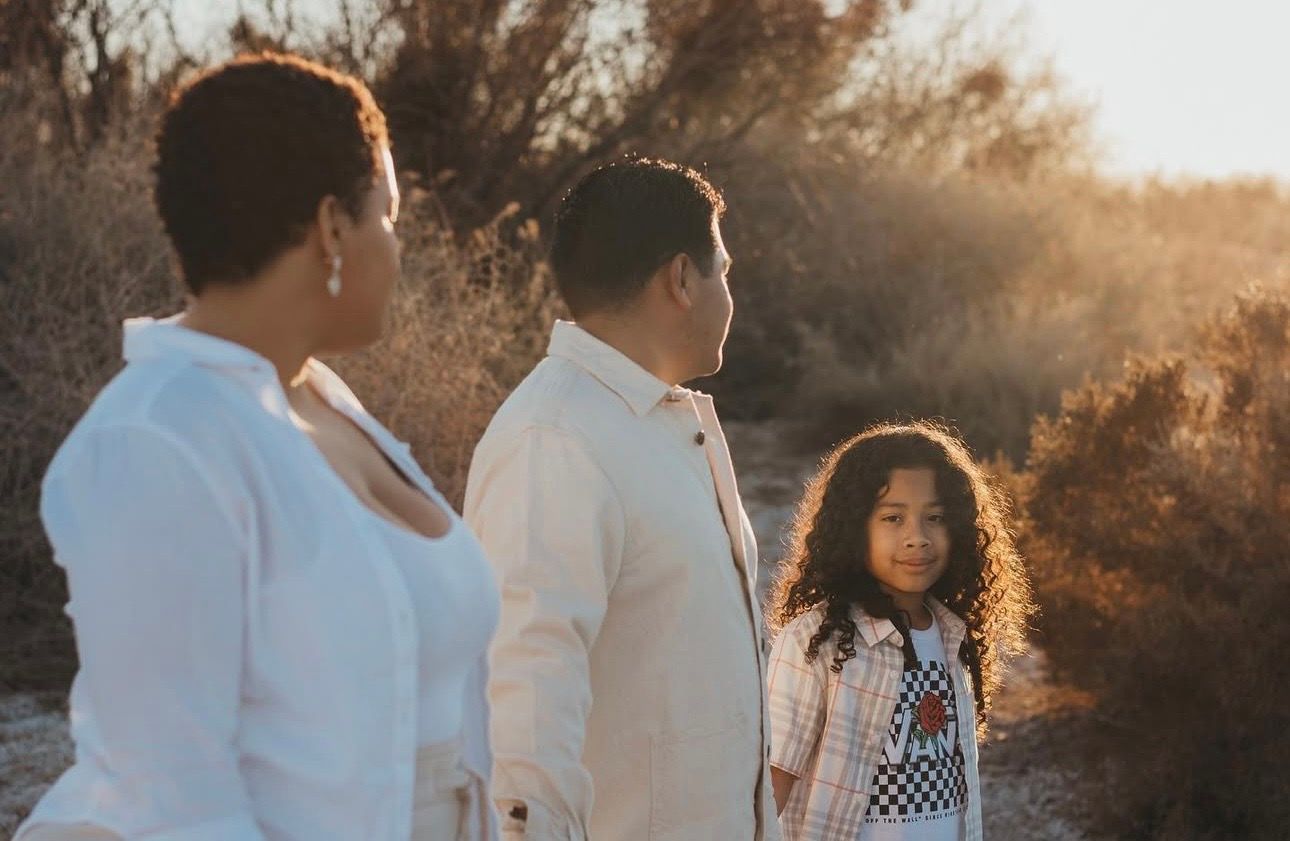 A young girl with curly hair stands beside two adults in a sun-drenched desert landscape.