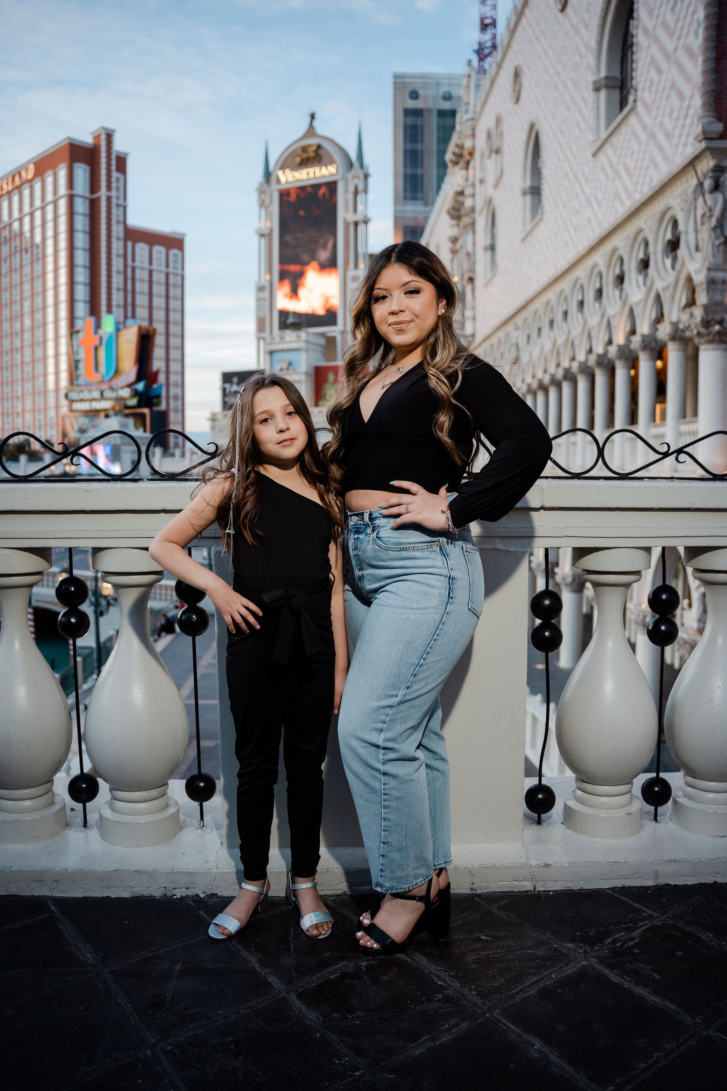 Two females in black outfits pose on a balcony with the Las Vegas Strip skyline in the background.