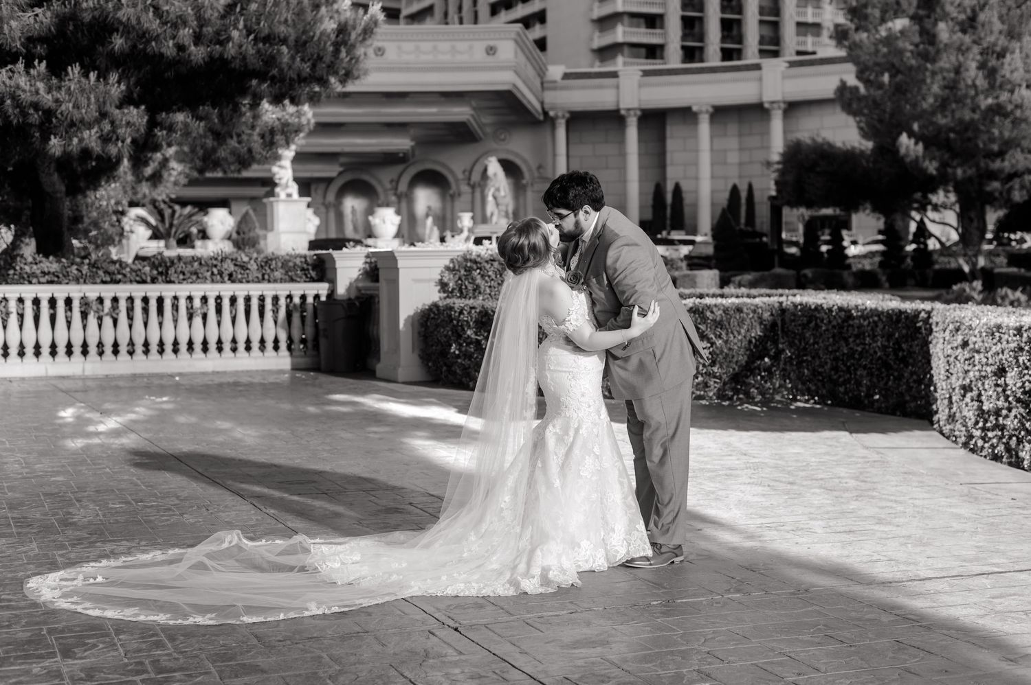 Black and white photo of bride and groom sharing a romantic kiss outdoors at an elegant venue.
