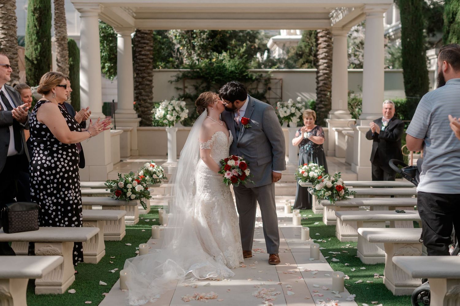 Bride and groom kiss at the end of the aisle as guests applaud at outdoor garden wedding.