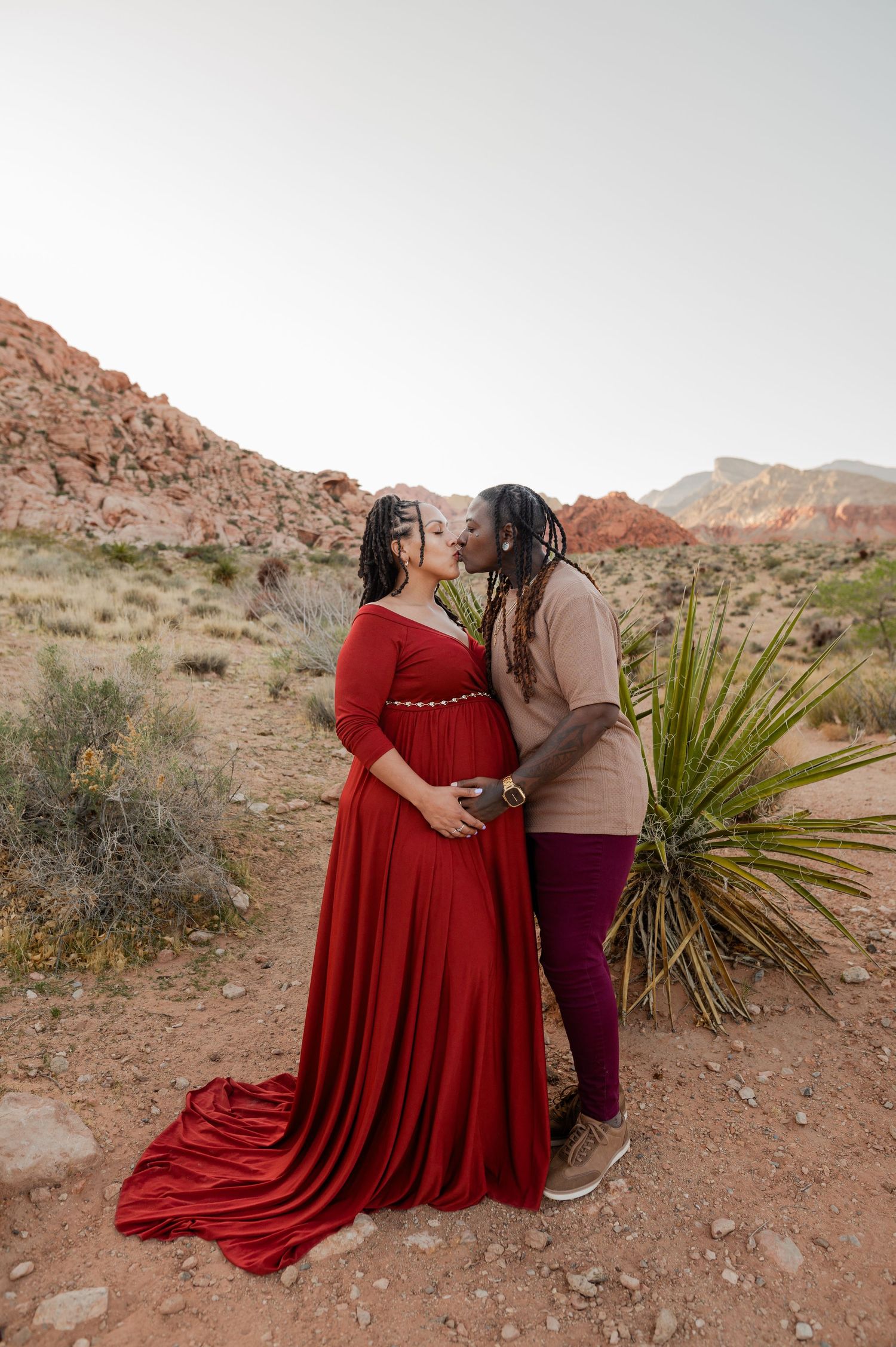 Pregnant couple sharing a kiss during a maternity photoshoot at Red Rock Canyon in a stunning red gown.