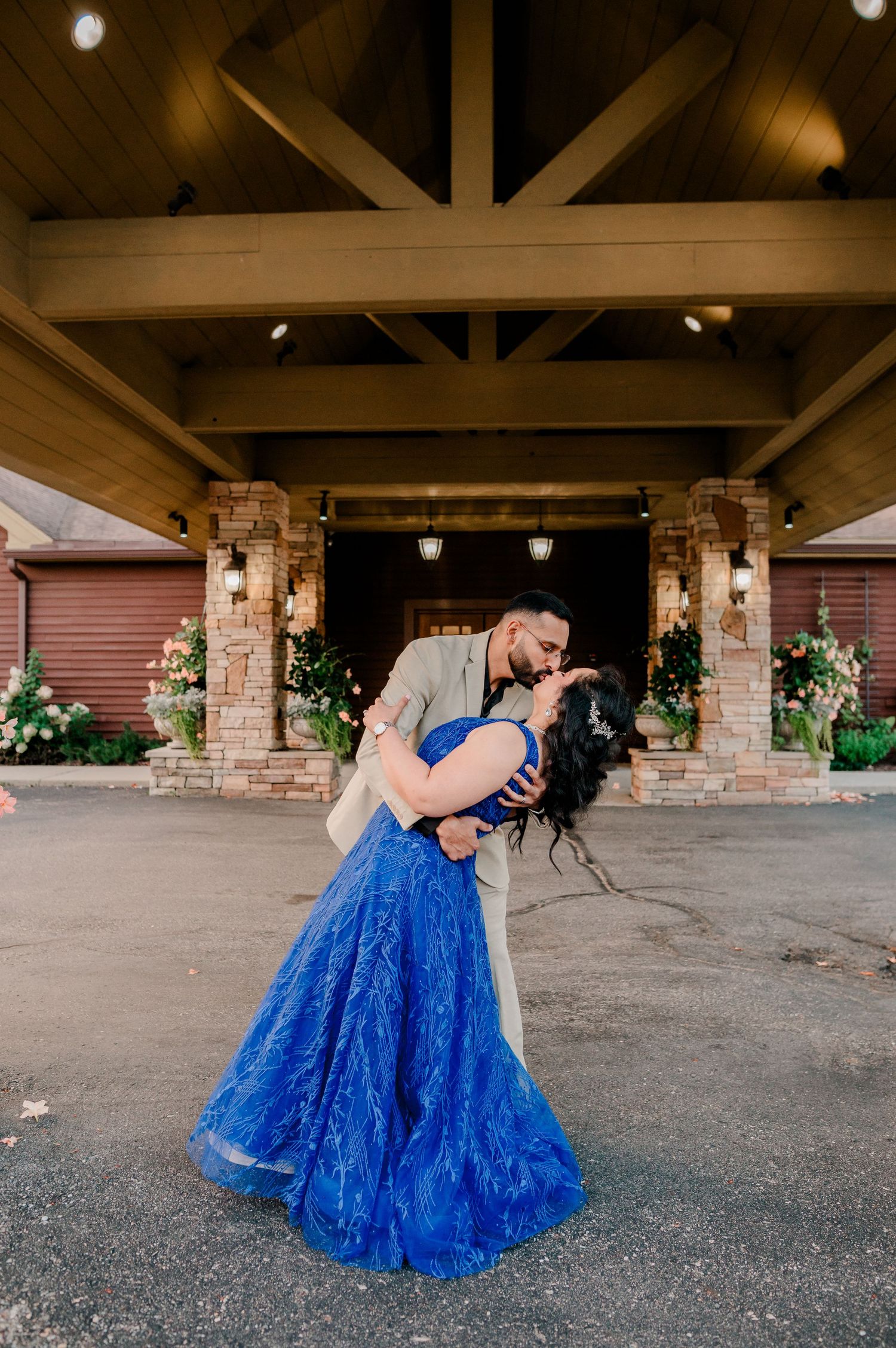 Couple sharing a romantic dip kiss under a wooden pavilion, woman in a stunning royal blue ball gown.