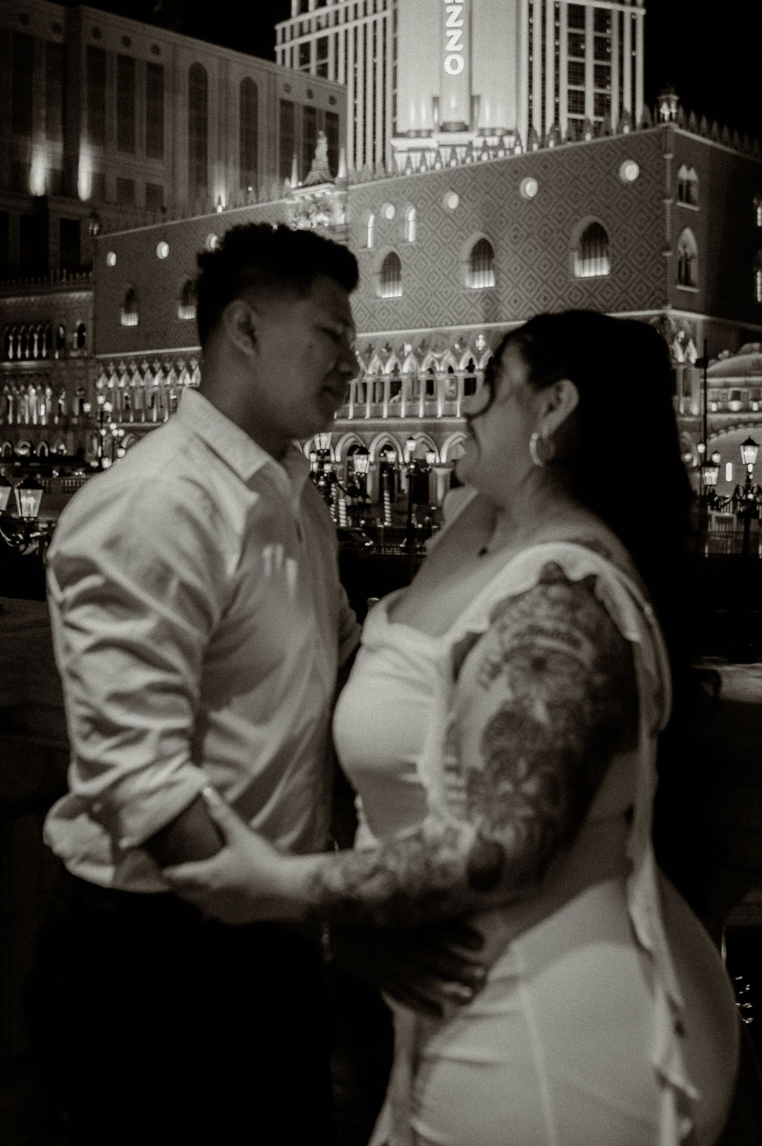 Black and white romantic photo of a couple embracing at night in front of the Venetian in Las Vegas.