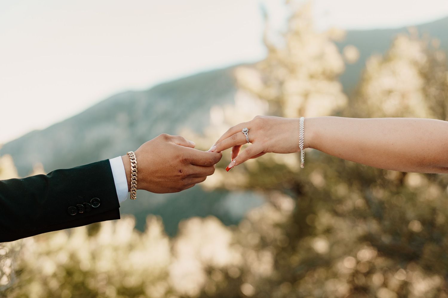 Close-up of couple exchanging rings with a scenic mountain and lake background.