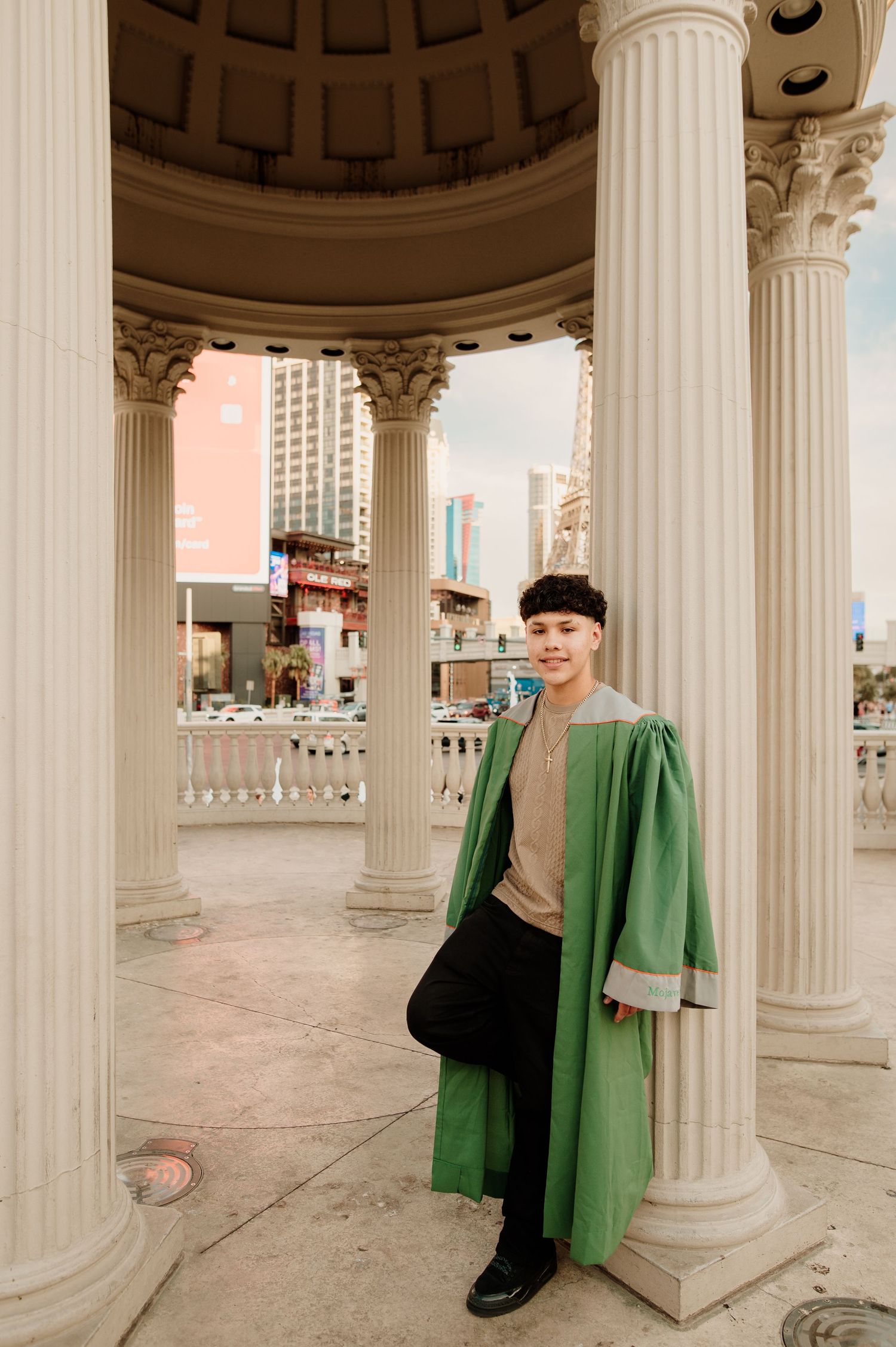 Graduate in green gown posing between white Roman columns at Caesars Palace Las Vegas.