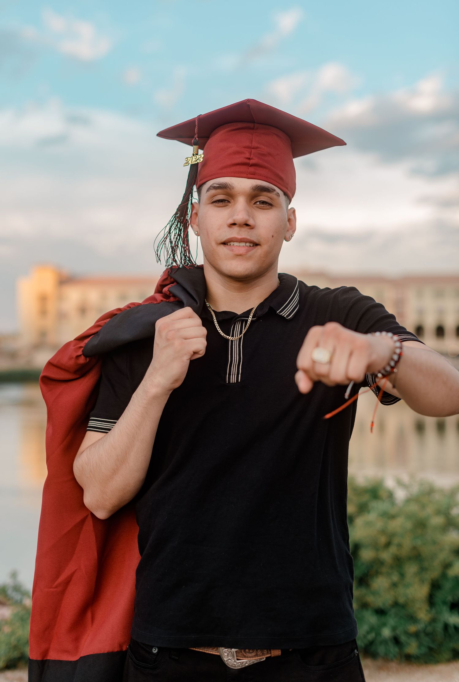 Smiling graduate in red mortarboard pointing forward with gown draped over shoulder.