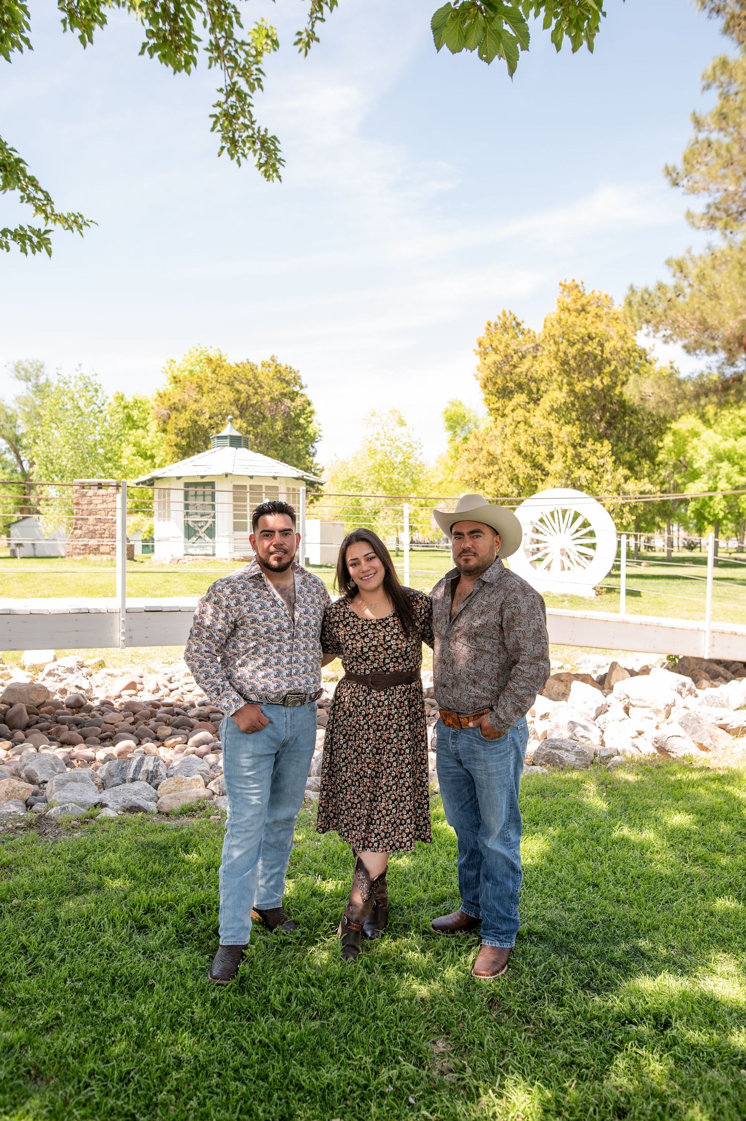 Three siblings in western attire posing together in a sunny green park.