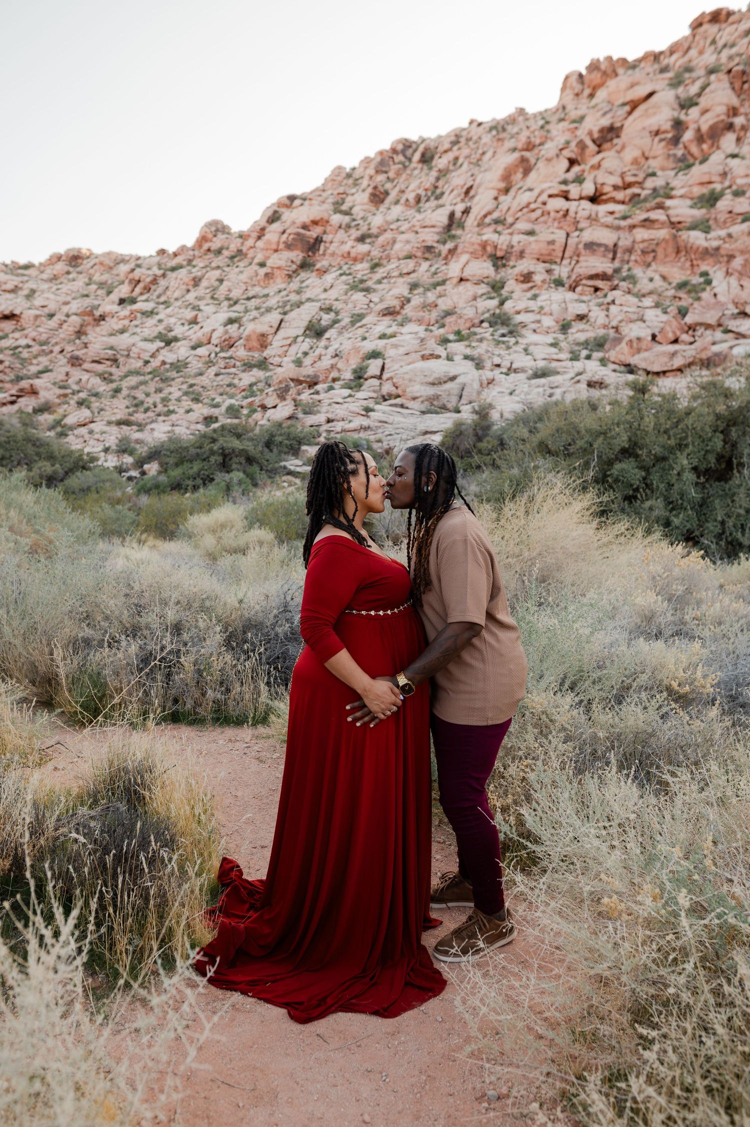 Couple sharing a kiss amid desert brush during Red Rock Canyon maternity photo session.