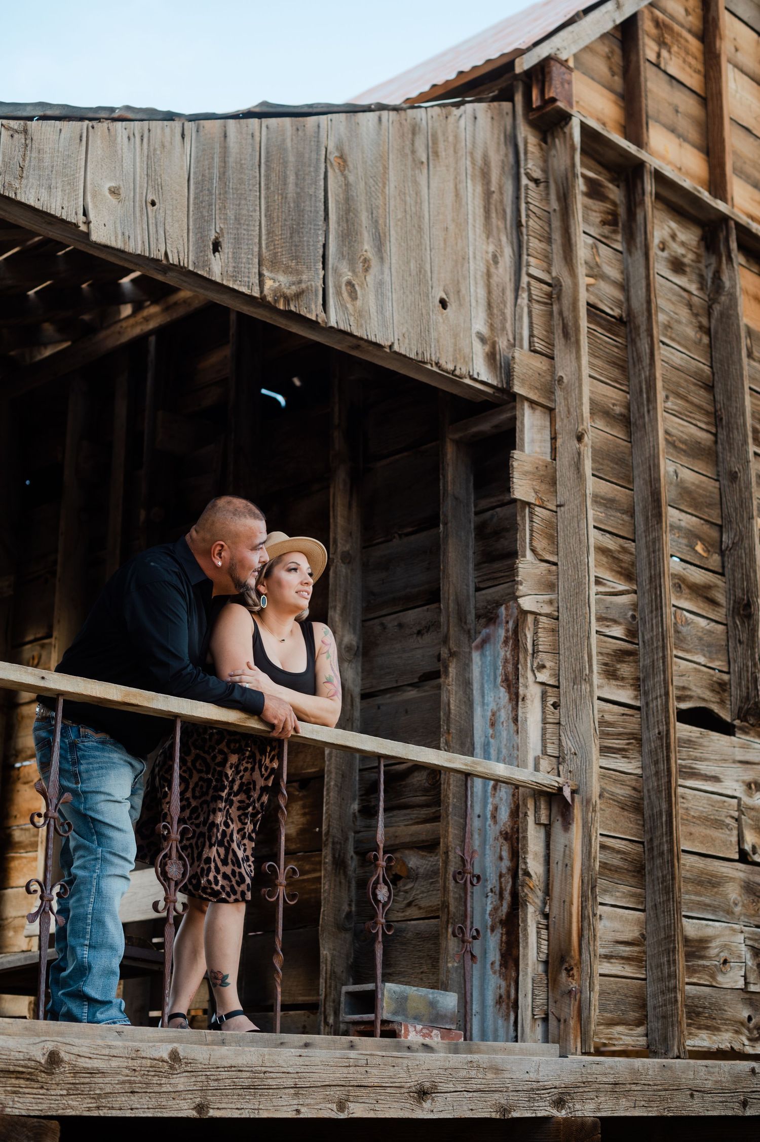 Couple standing together on a rustic wooden balcony of an old barn, gazing into the distance.