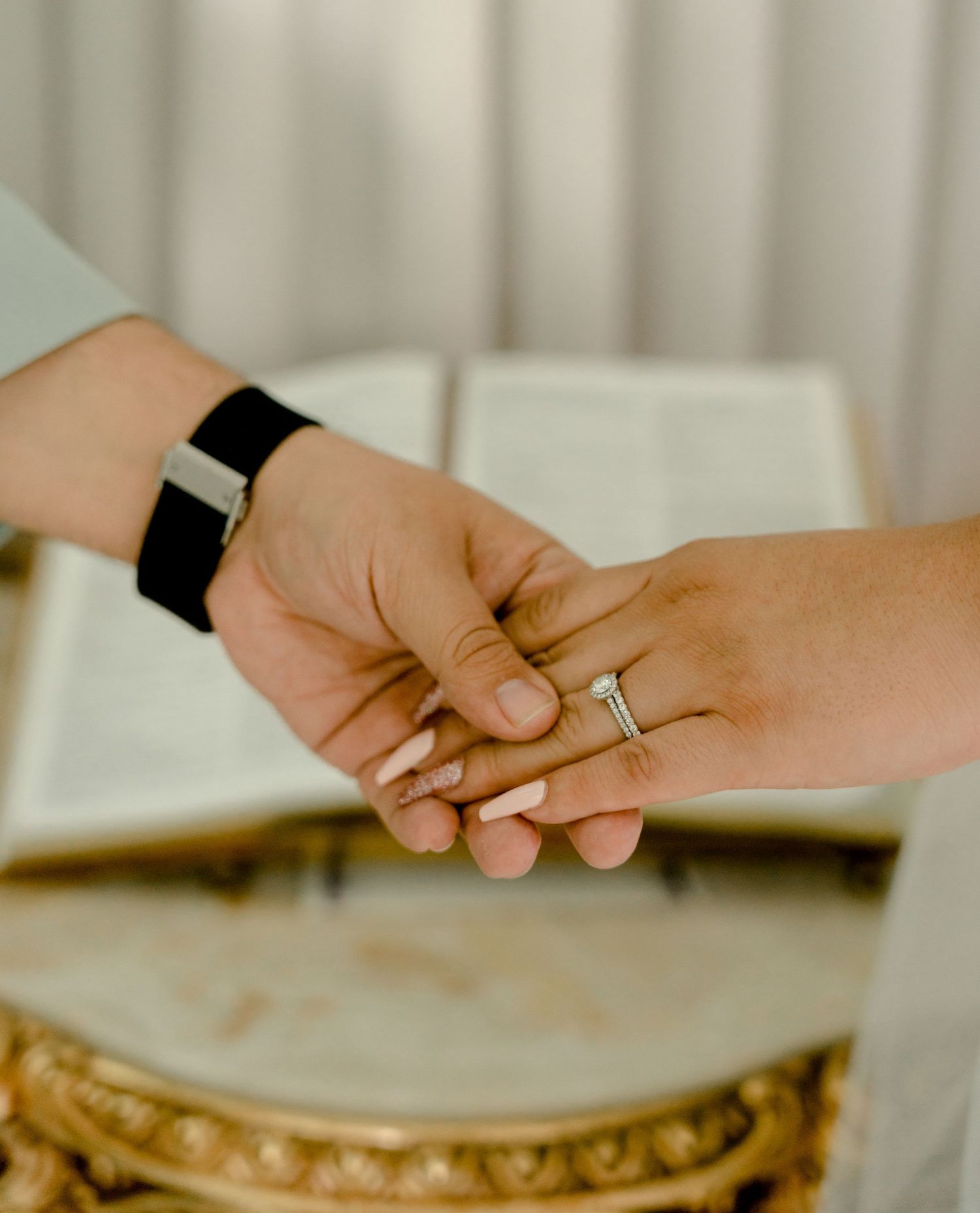 Close-up of groom placing diamond wedding ring on bride's hand over ornate gold table with open Bible.