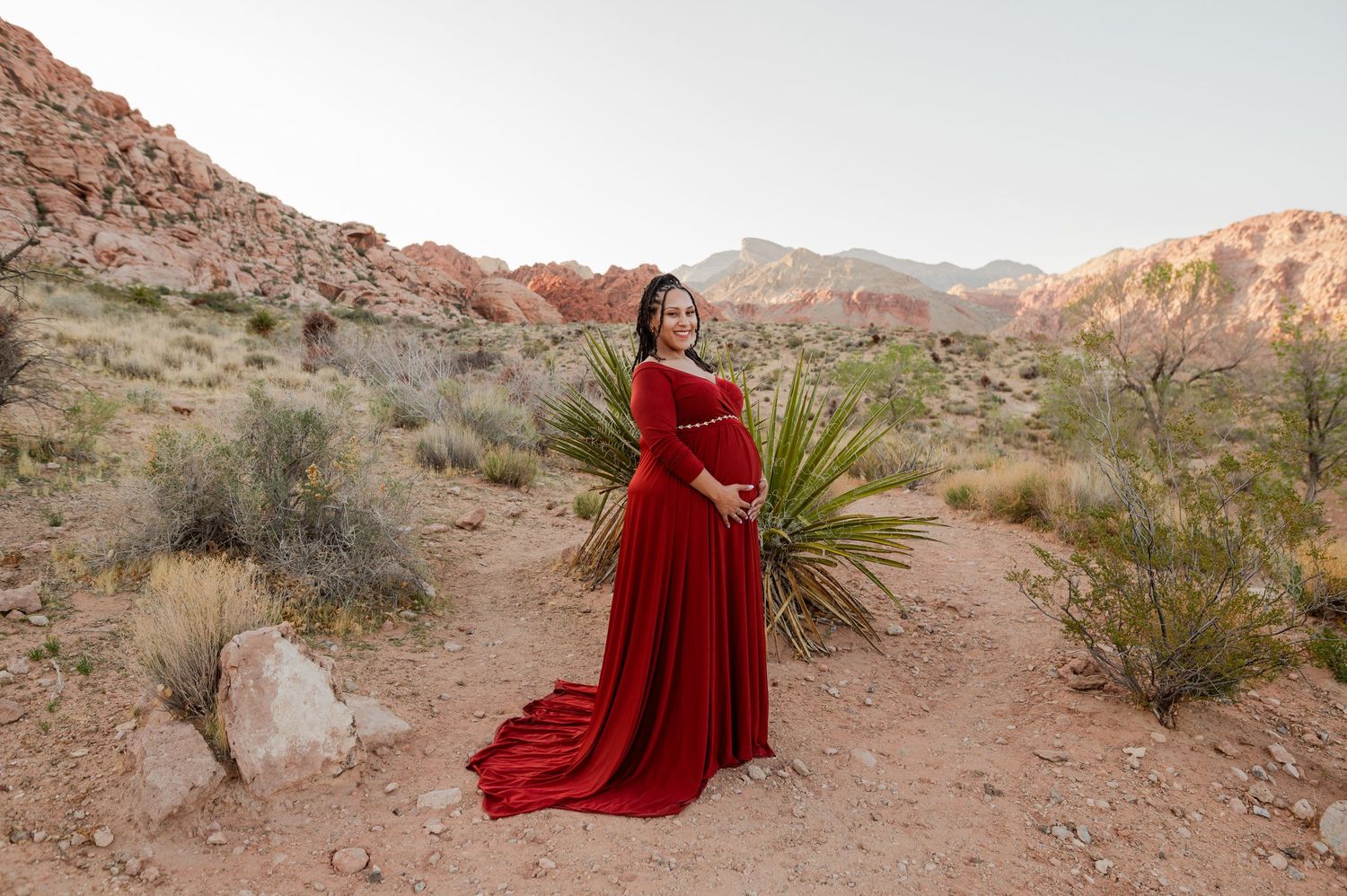 Expectant mother in dramatic red maternity dress standing among desert yucca plants at Red Rock Canyon.