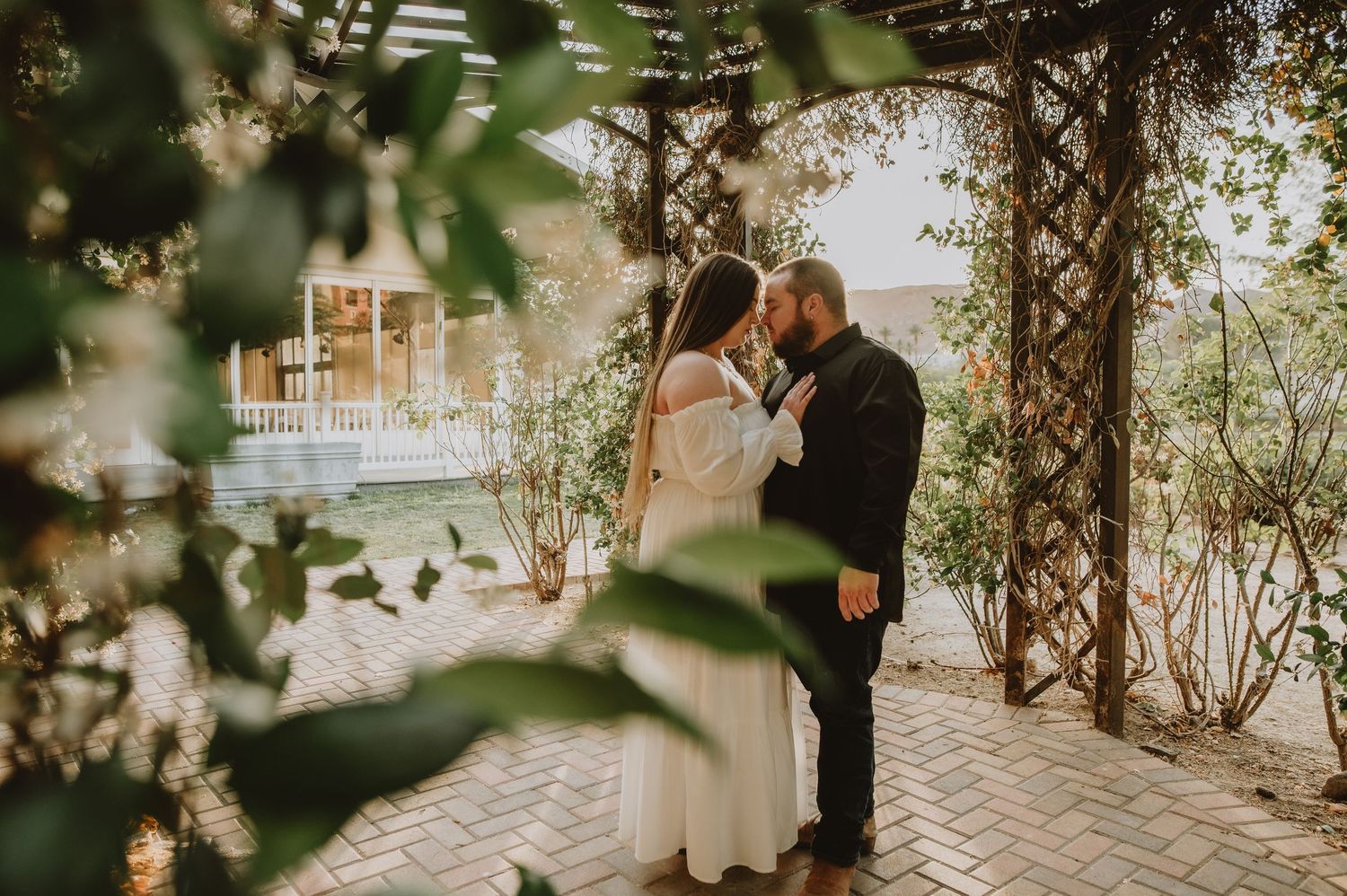 Bride and groom share intimate moment under vine-covered pergola at outdoor wedding venue.