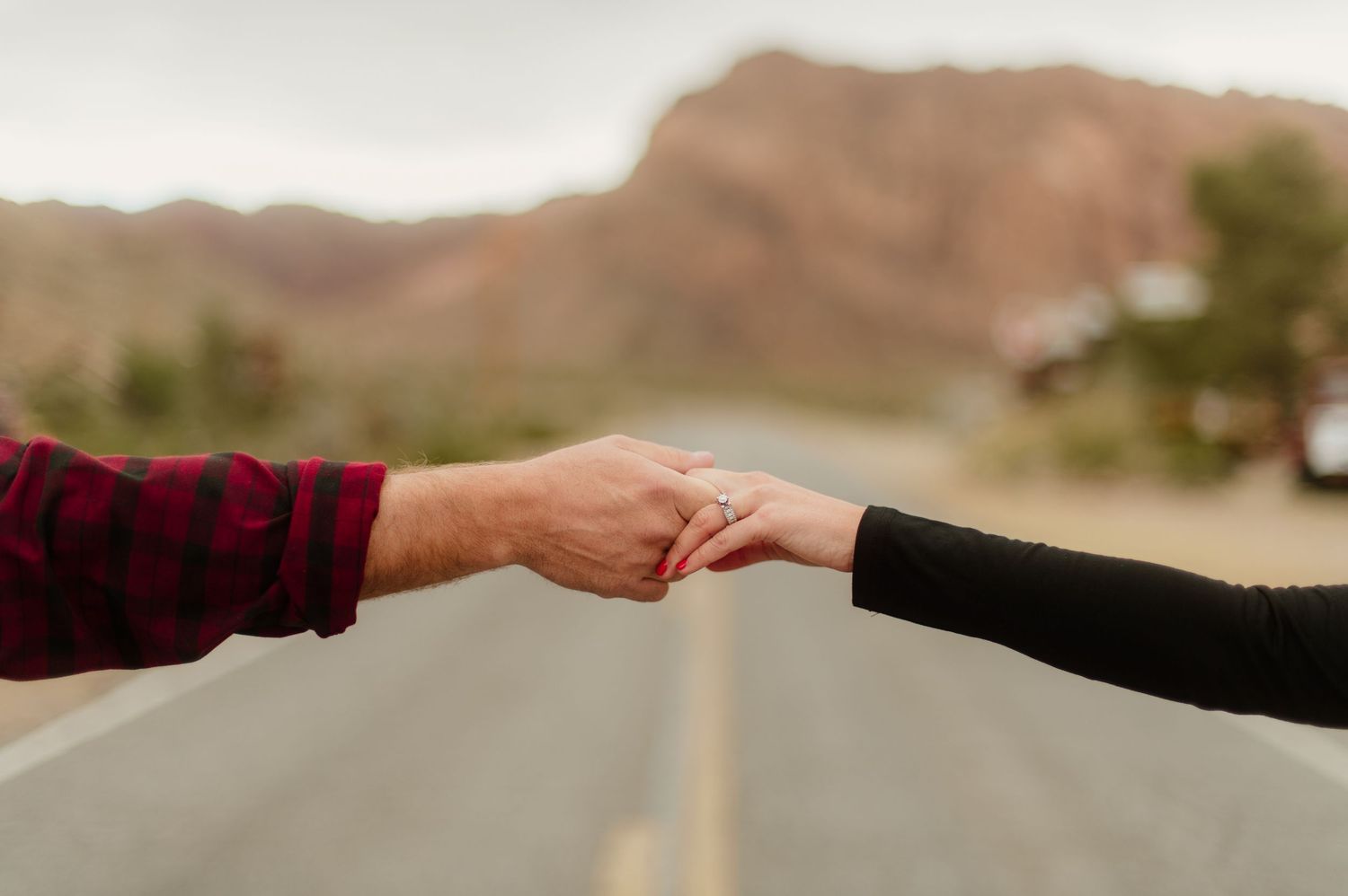 Close-up of couple holding hands on a desert road with mountains in the background.