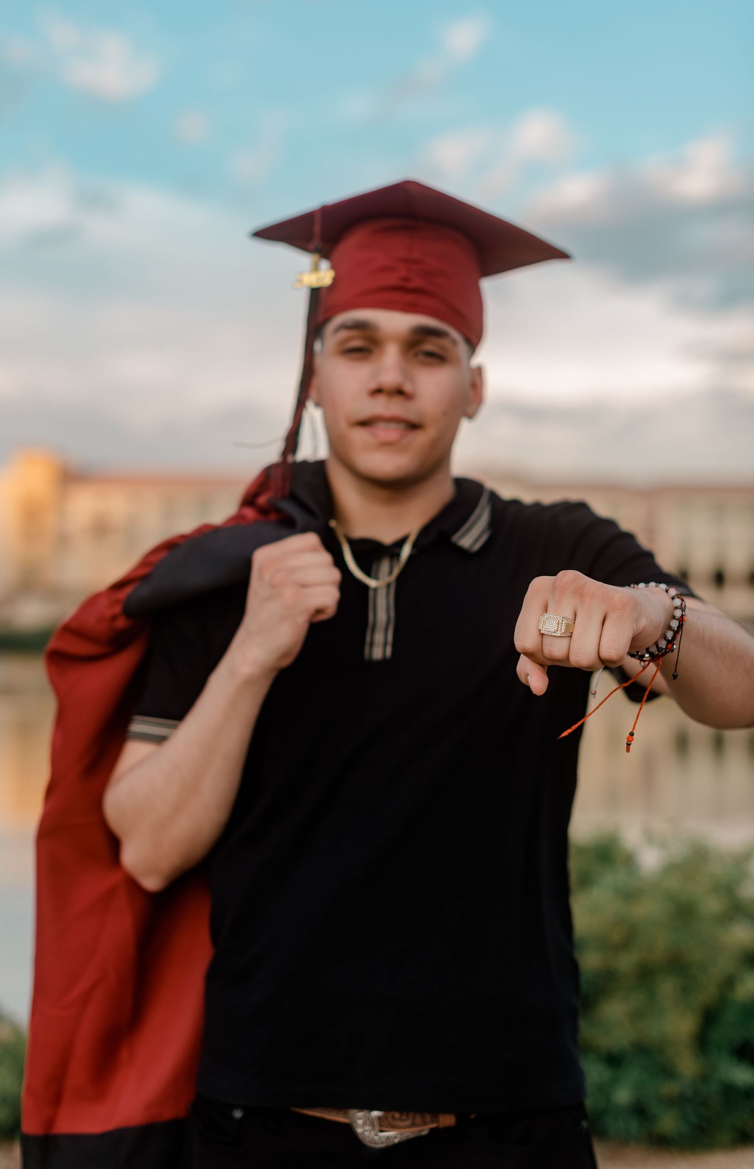 Young man in graduation cap pointing at camera with gown over shoulder.
