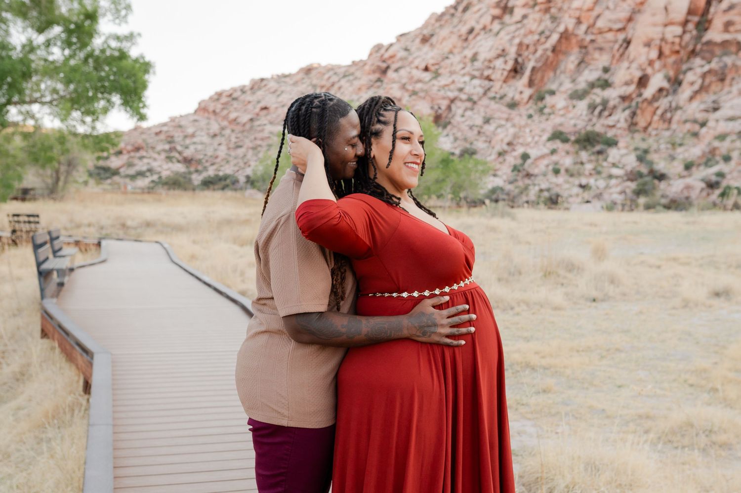 Two women embracing on wooden boardwalk during maternity shoot at Red Rock Canyon.