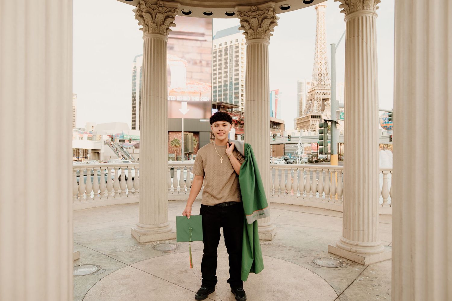 Young male graduate holding green gown among white pillars at Caesars Palace Las Vegas.