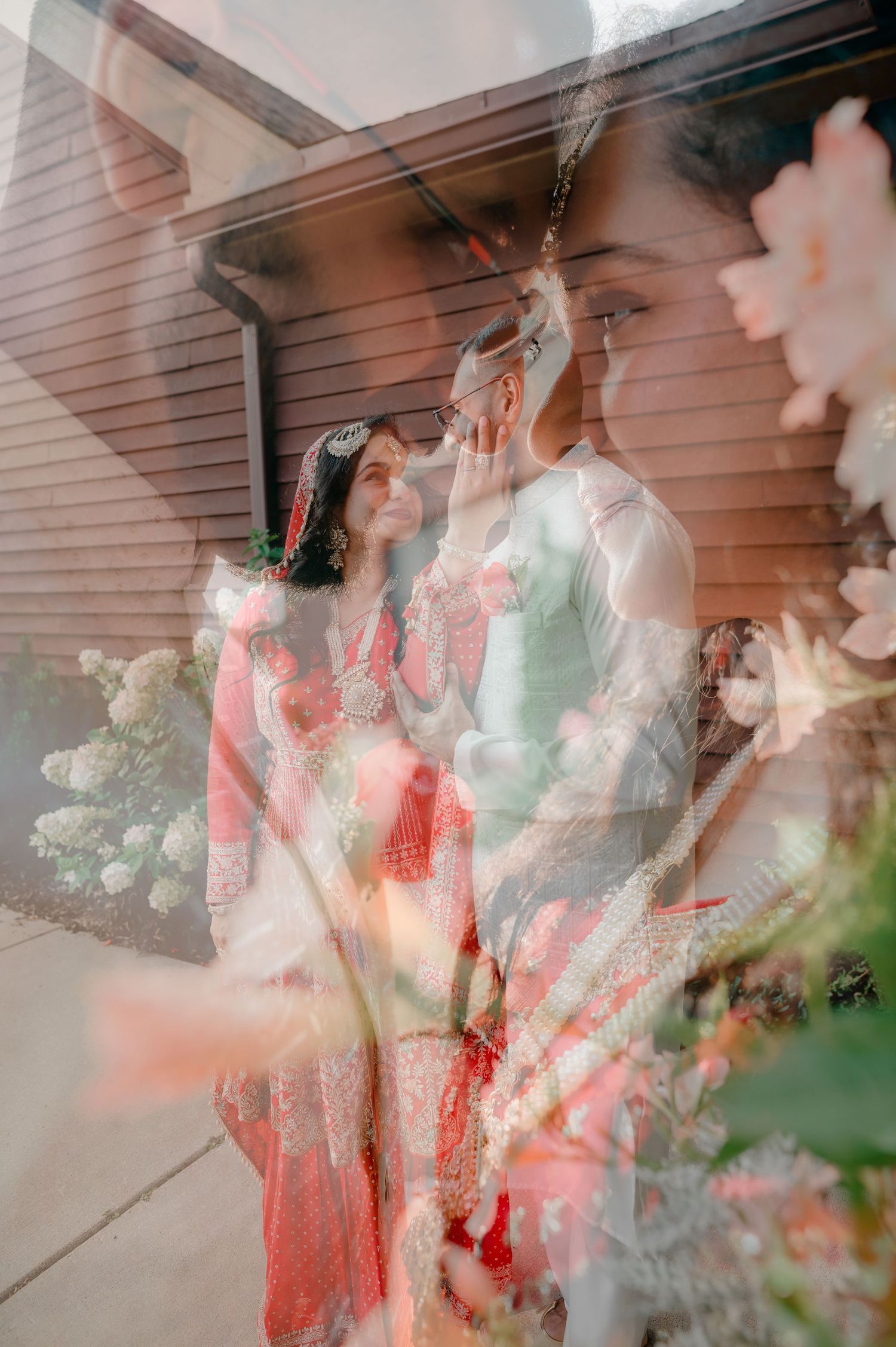 Double exposure photo of a couple in traditional South Asian wedding attire surrounded by blooming flowers.