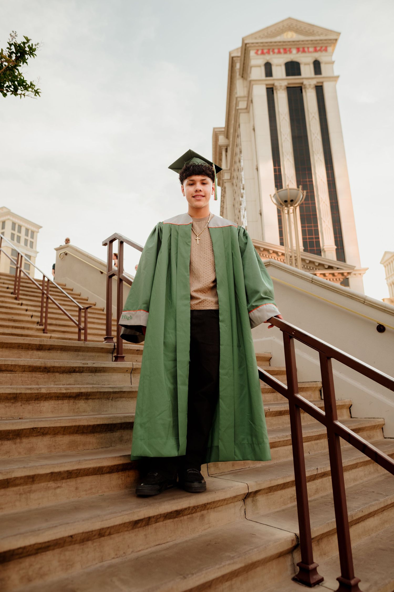 Young male graduate in green gown and cap on Caesars Palace steps in Las Vegas.