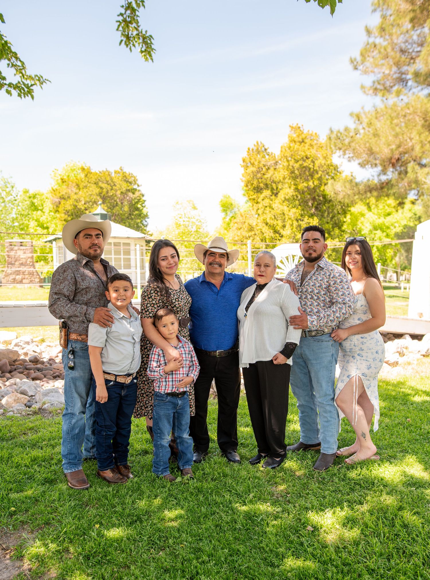 Extended Hispanic family of seven poses together on green lawn with trees in background.