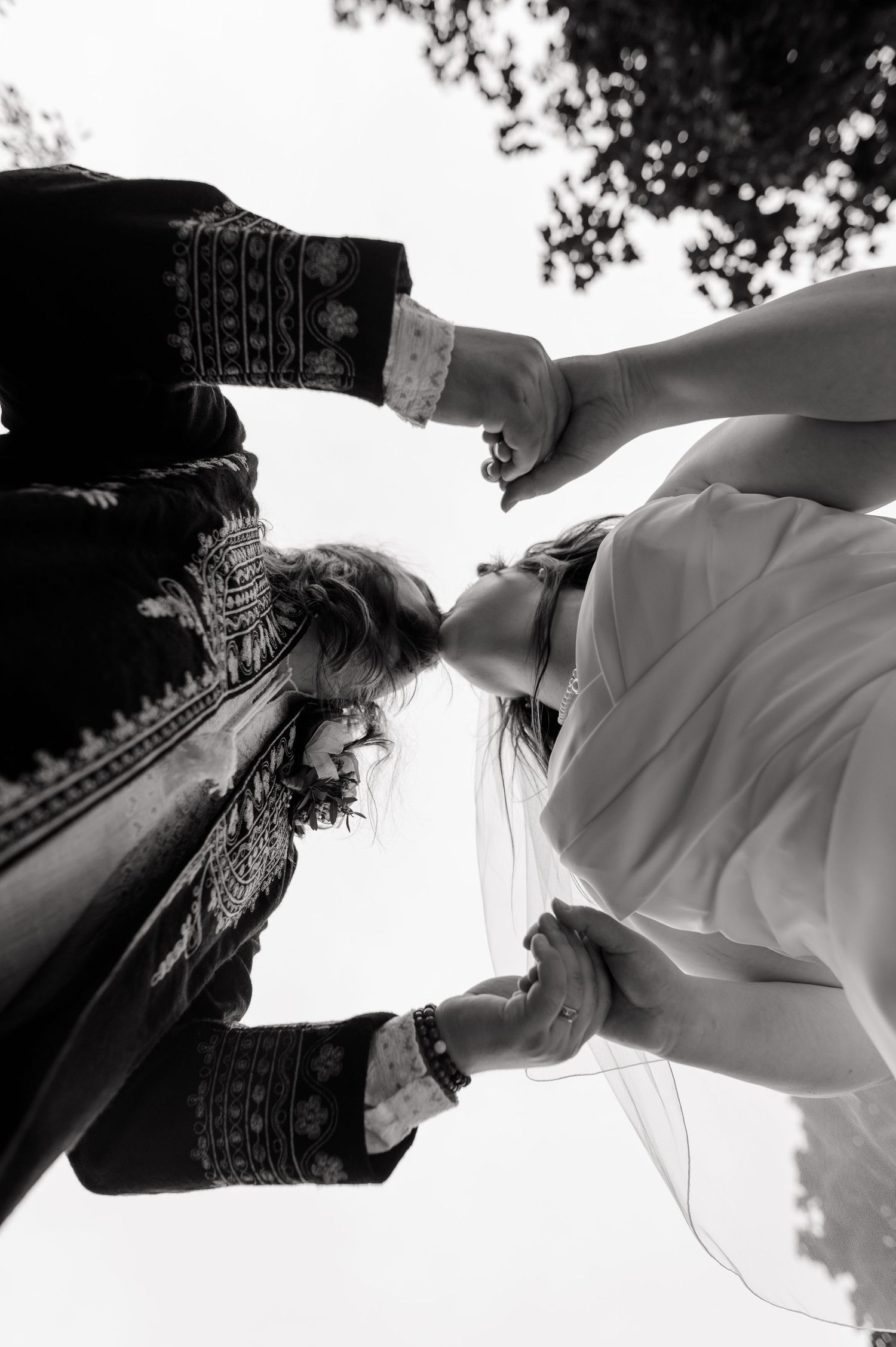 Black and white low angle shot of bride and groom holding hands and kissing outdoors on wedding day.
