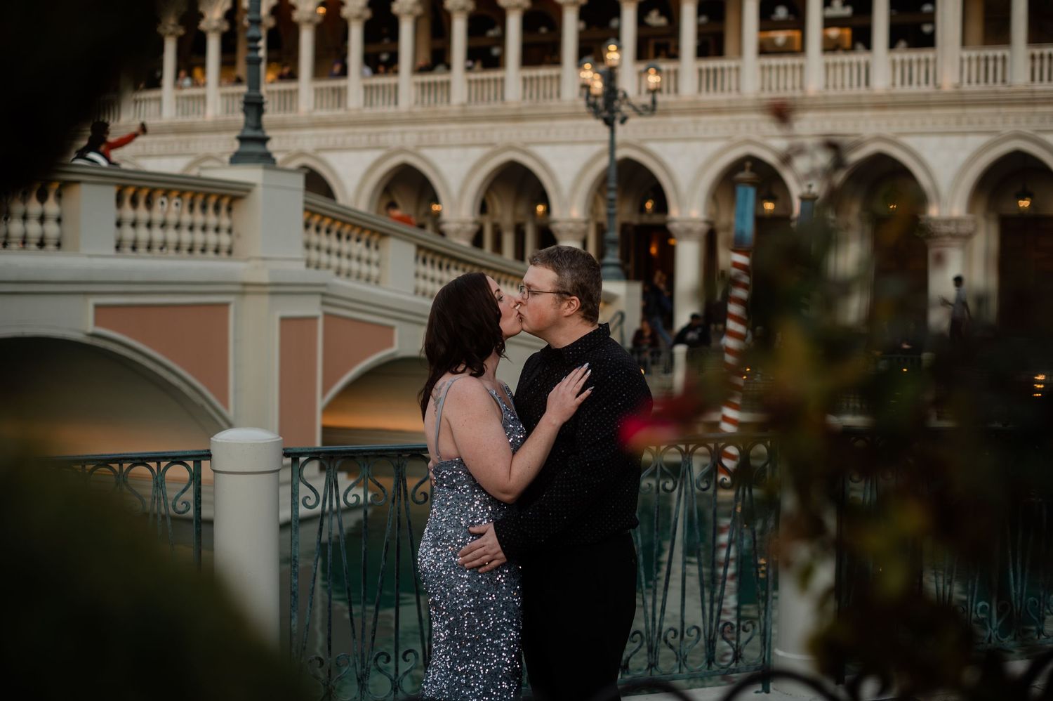 Couple shares a kiss near the Venetian gondola bridge during romantic evening engagement session.