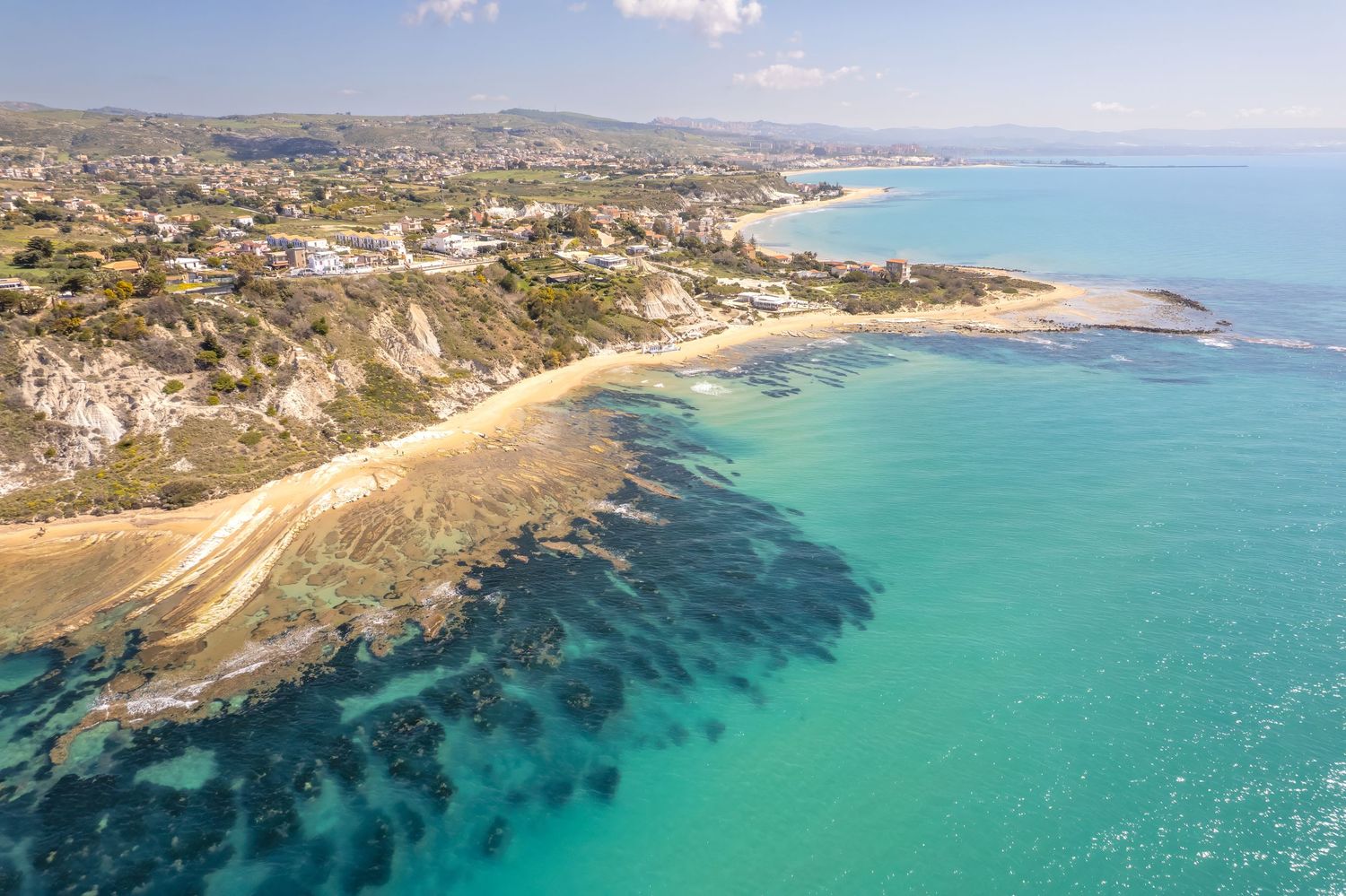 Aerial view of a stunning turquoise coastline with sandy beaches, rocky shores, and a scenic Mediterranean town.