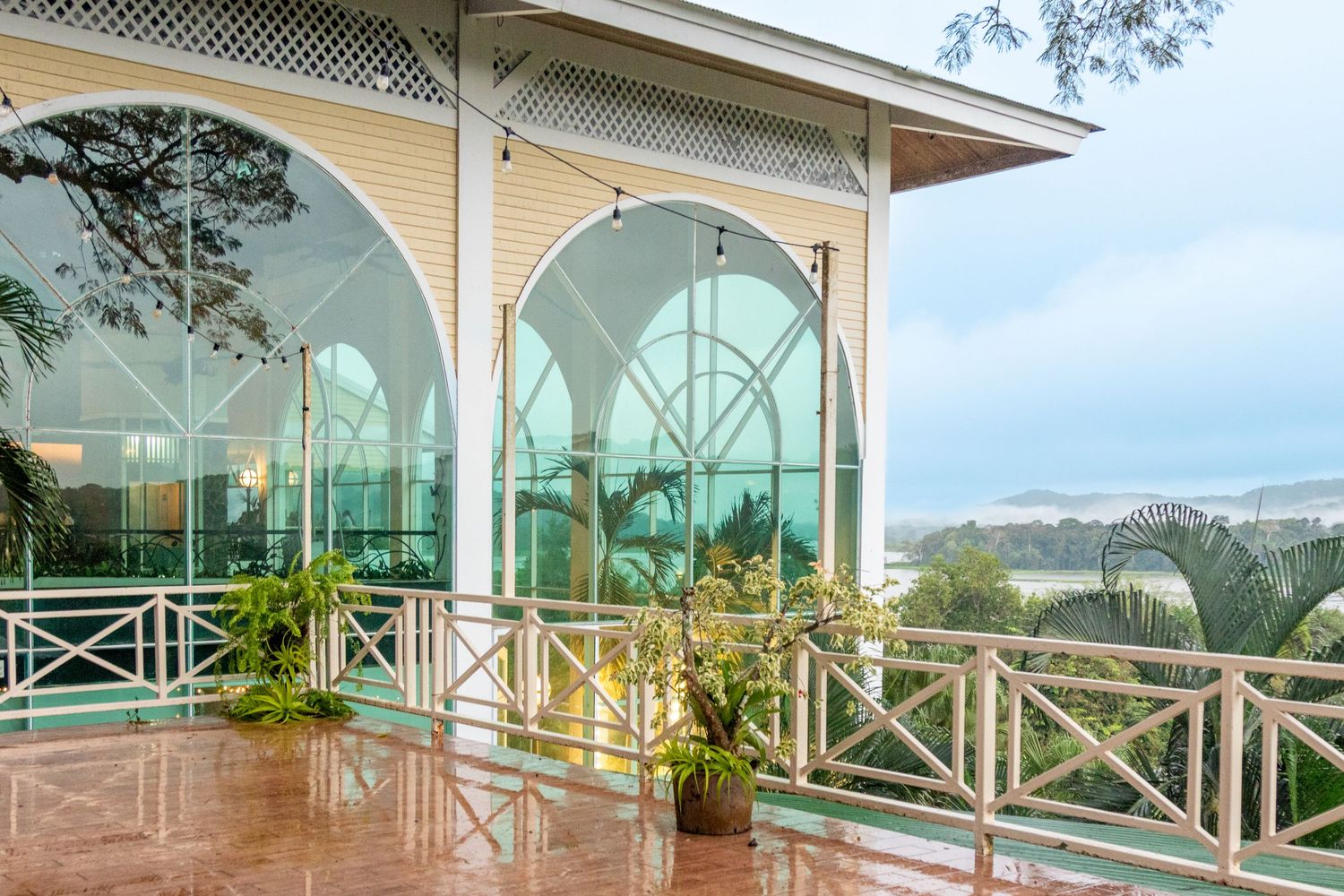 Elegant colonial veranda with arched glass windows overlooking tropical landscape and ocean view.