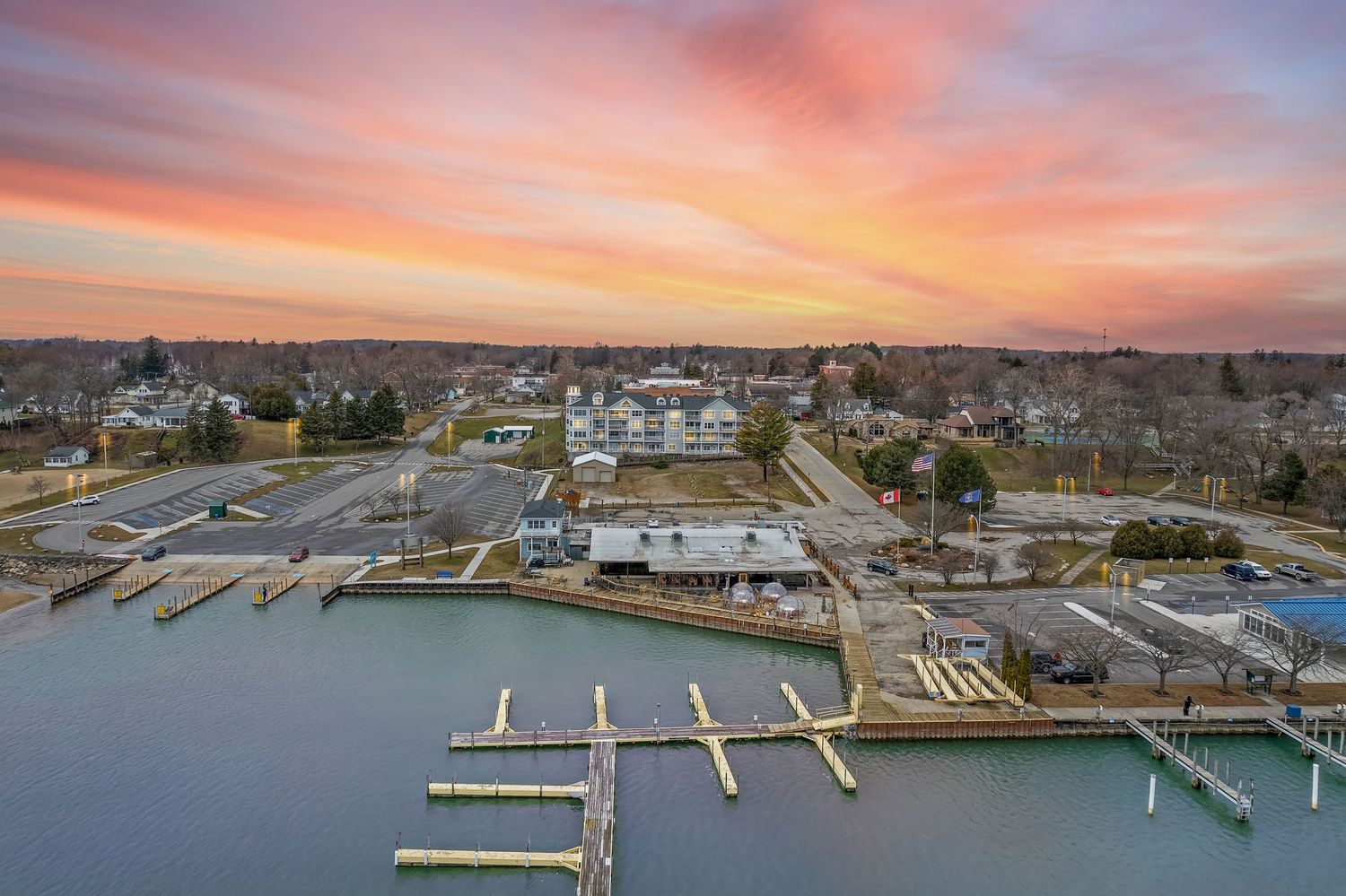 Aerial view of a marina with boat docks at sunset, overlooking a small waterfront town.