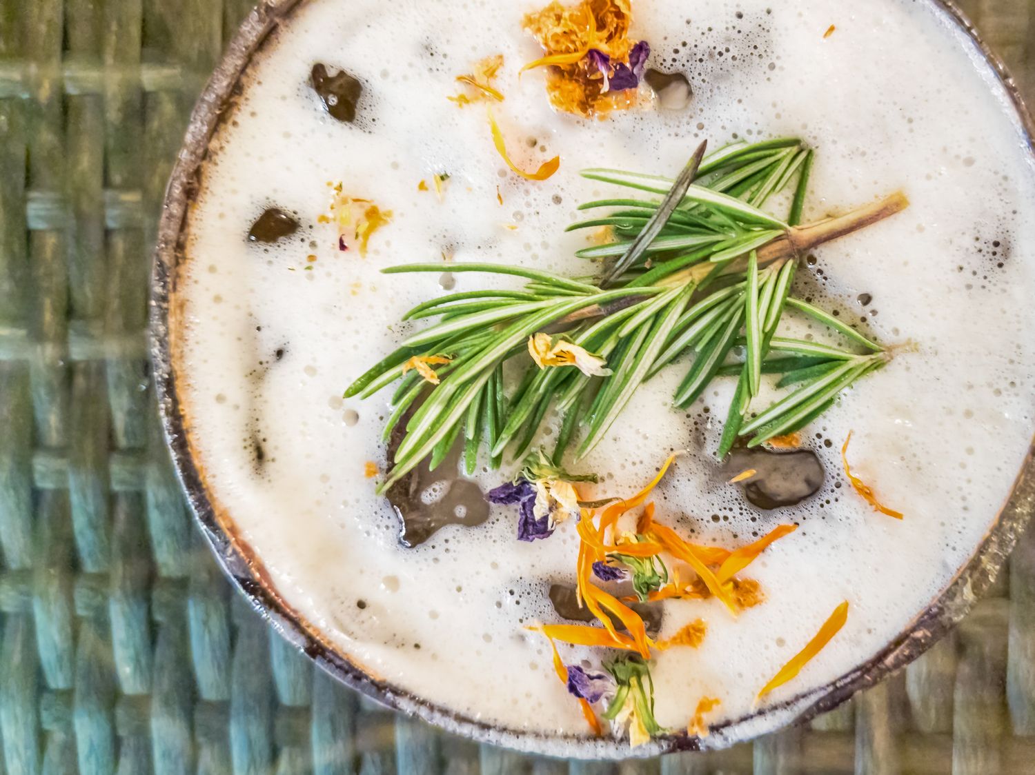 Creamy herbal cocktail topped with fresh rosemary sprigs and dried edible flowers in a rustic bowl.