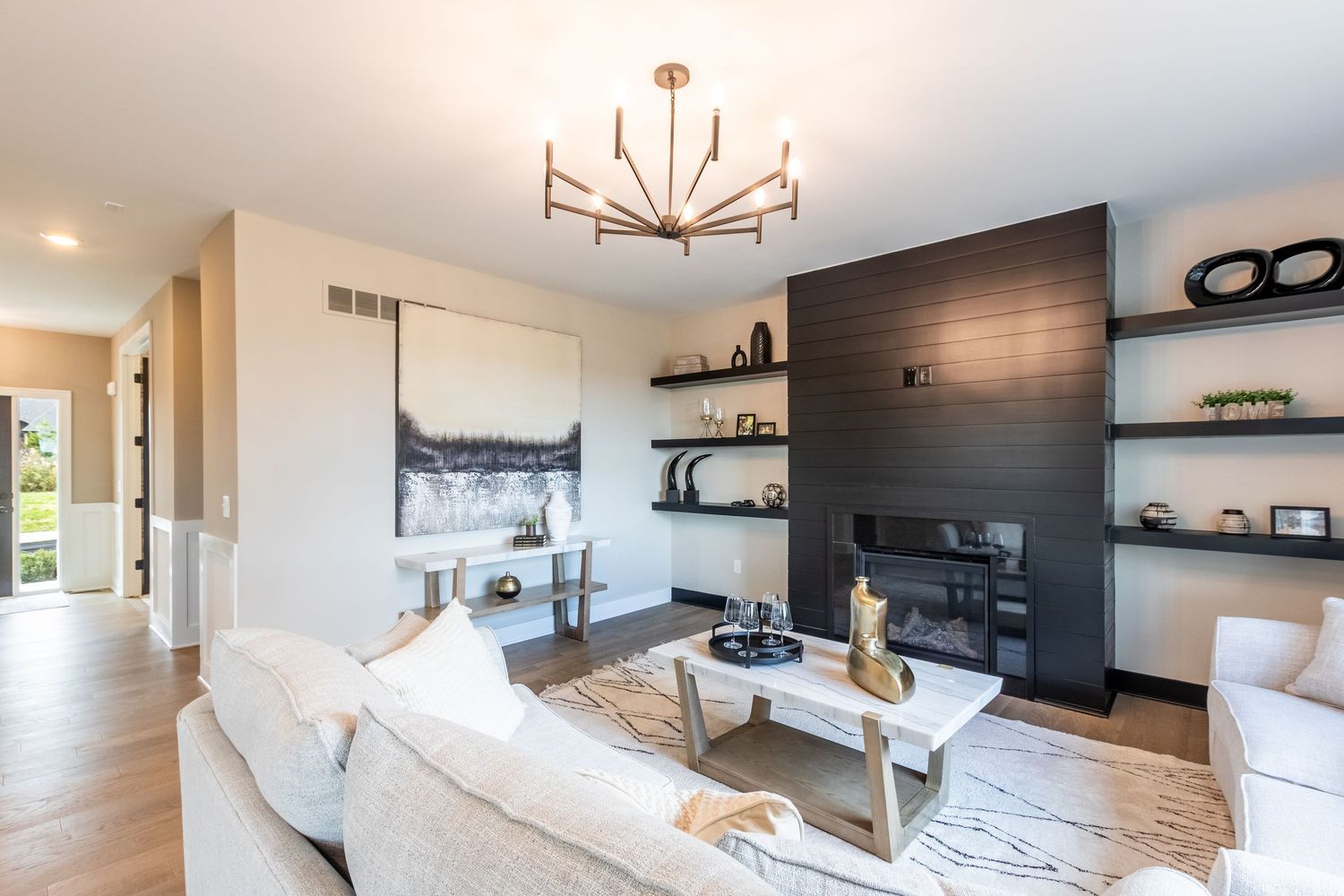 Modern living room with white sectional sofa, dark wood accent wall, built-in shelves, and contemporary sputnik chandelier.