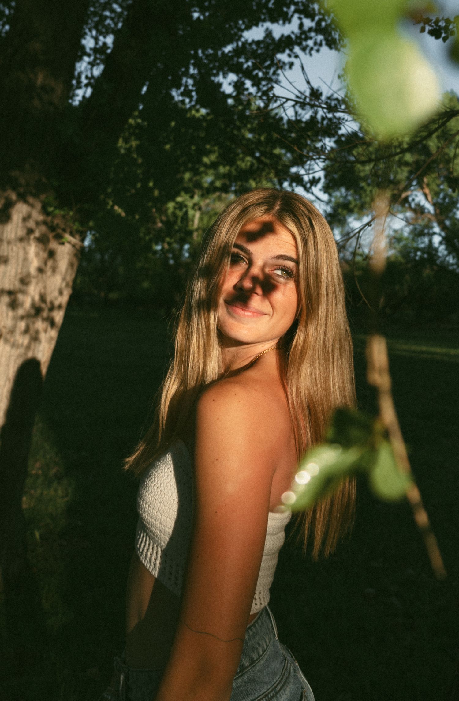Artistic portrait capturing golden hour lighting through tree leaves.